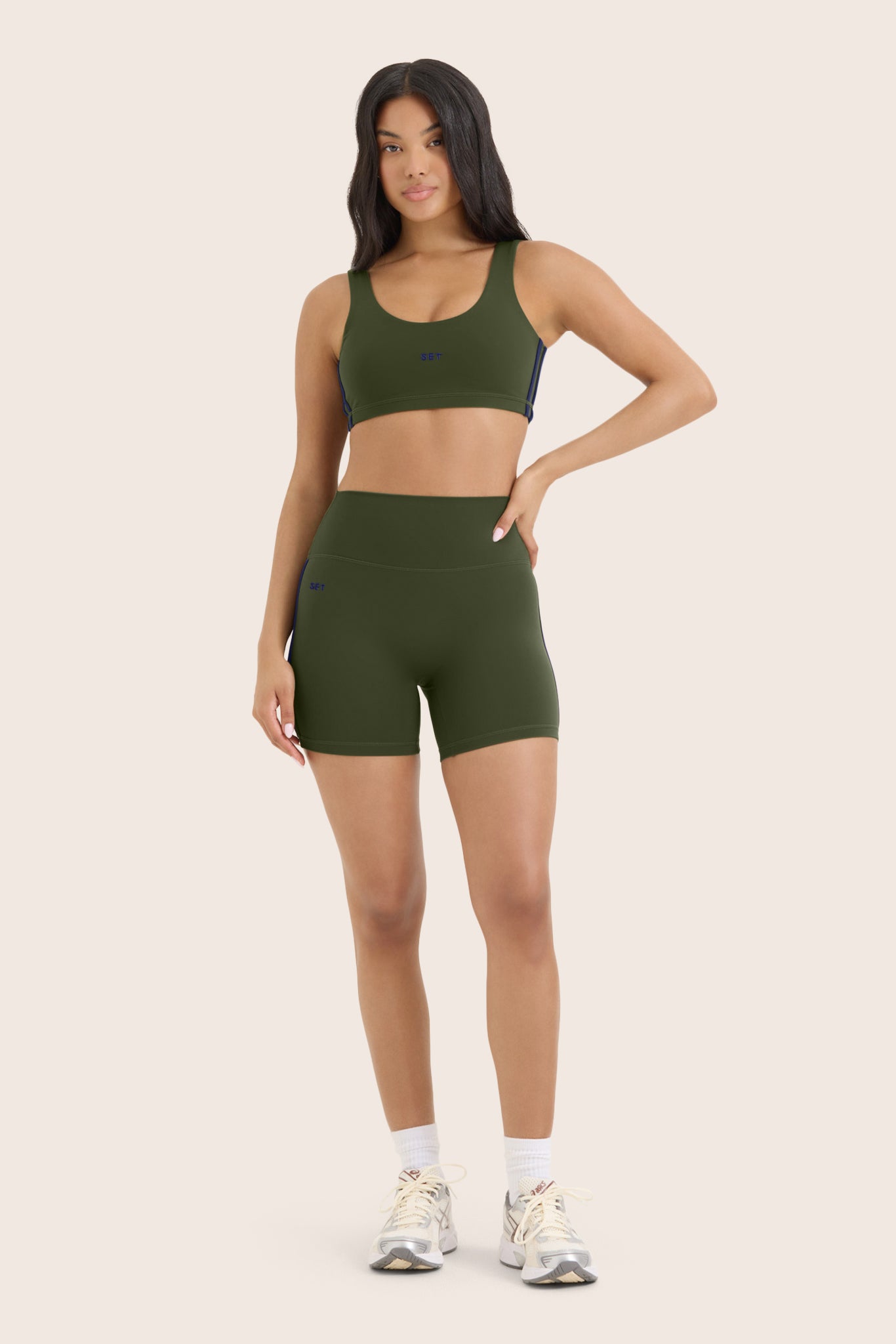 Woman wearing an olive green sports bra and shorts set on a beige background
