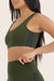 Woman wearing a green sports bra and leggings with a visible brand logo on a beige background 