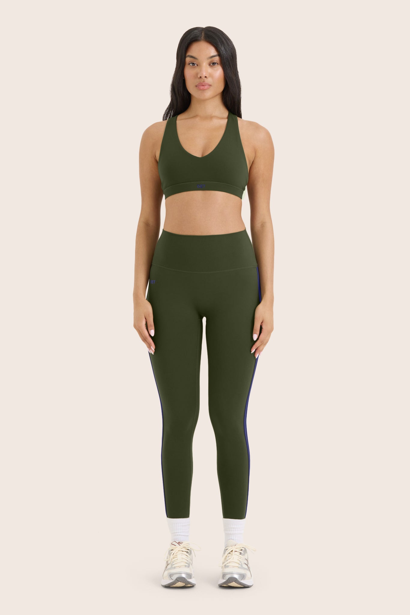 Woman wearing a green sports bra and leggings set on a beige background