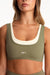 Green sports bra with white accents worn by a person on a plain background