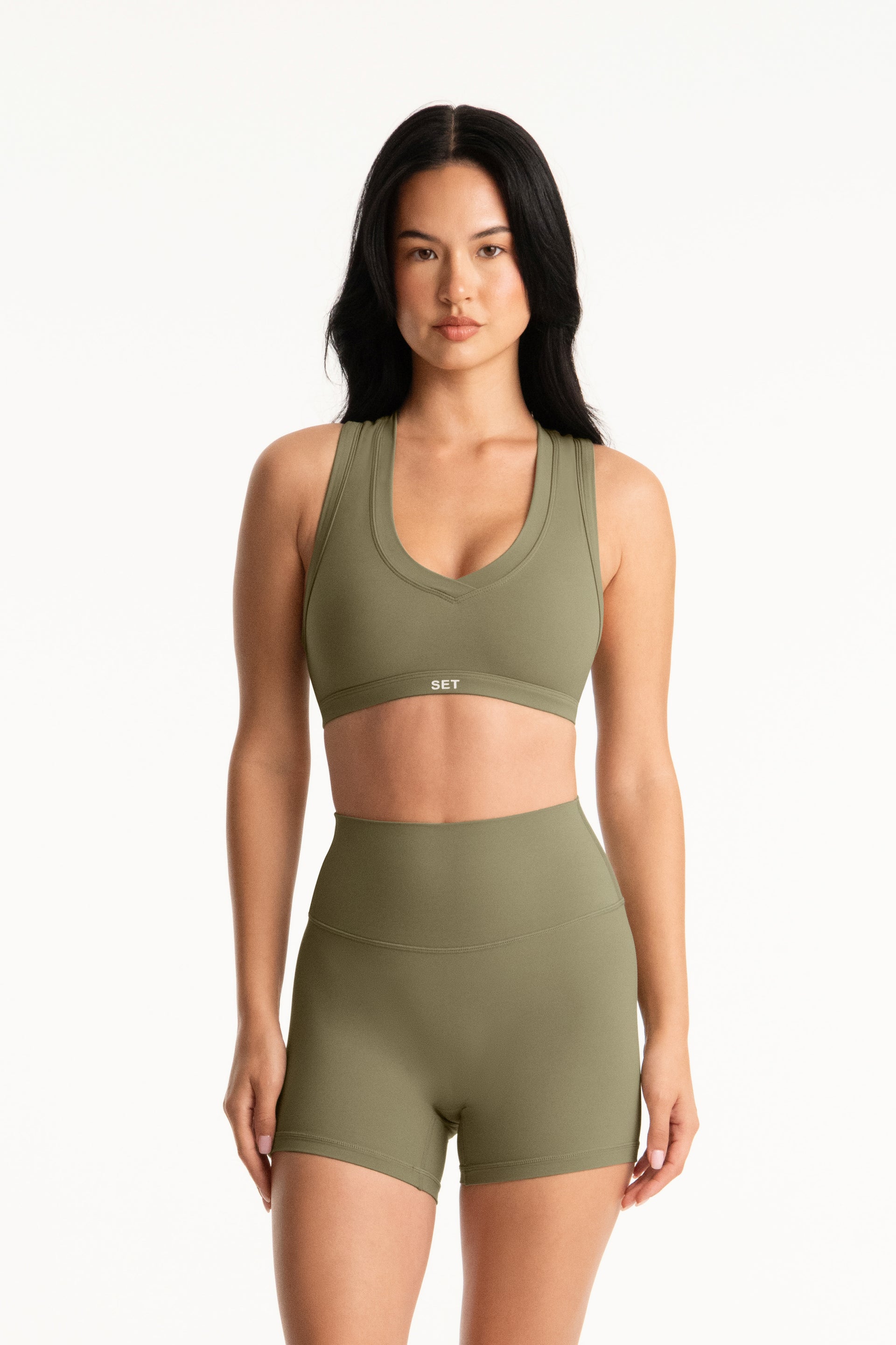 Woman wearing an olive green sports bra and shorts set on a white background <model-info>Jasmine wears a size S and is 5’8”, 25" waist, 36” bust.</model-info>