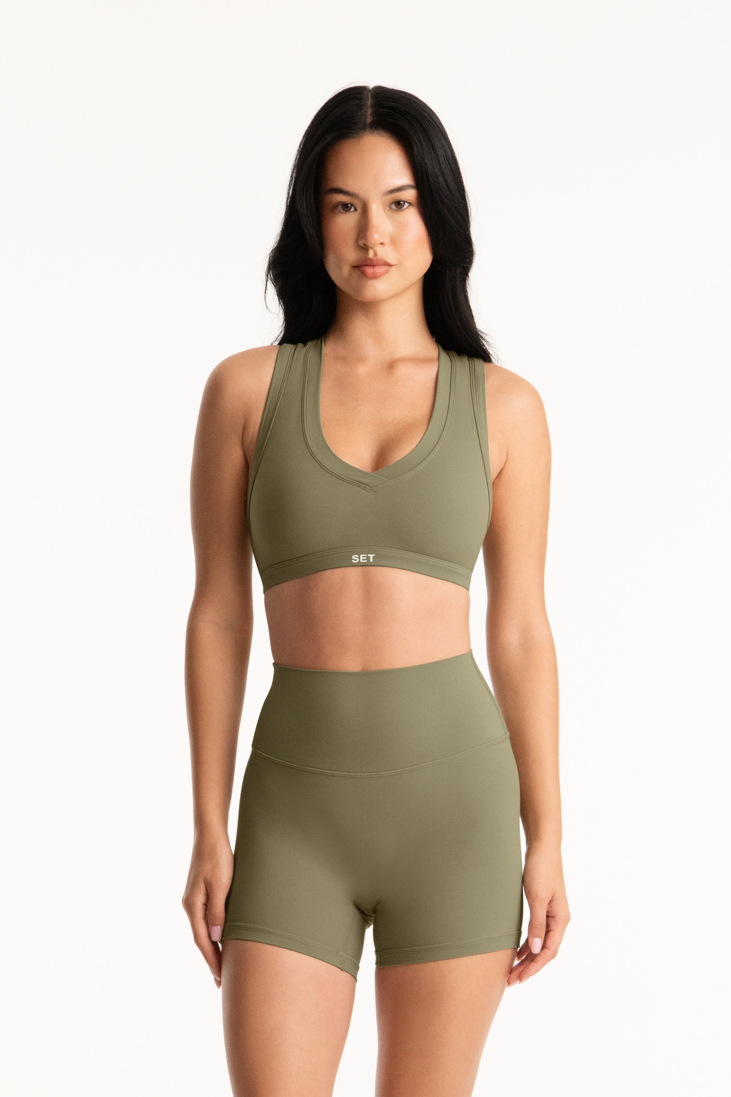 Woman wearing an olive green sports bra and shorts set on a white background 
