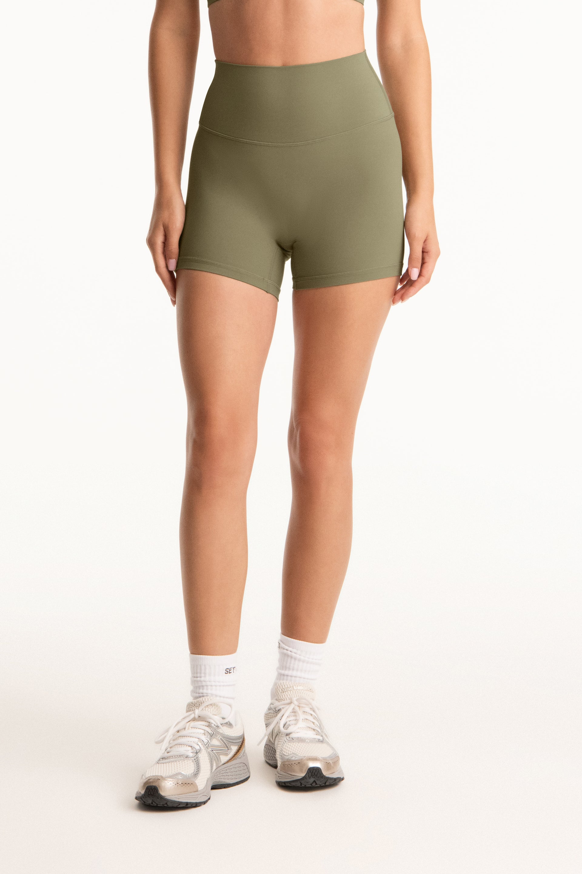 Person wearing olive green shorts on a white background <model-info>Jasmine wears a size S and is 5’8”, 25" waist, 36” bust.</model-info>