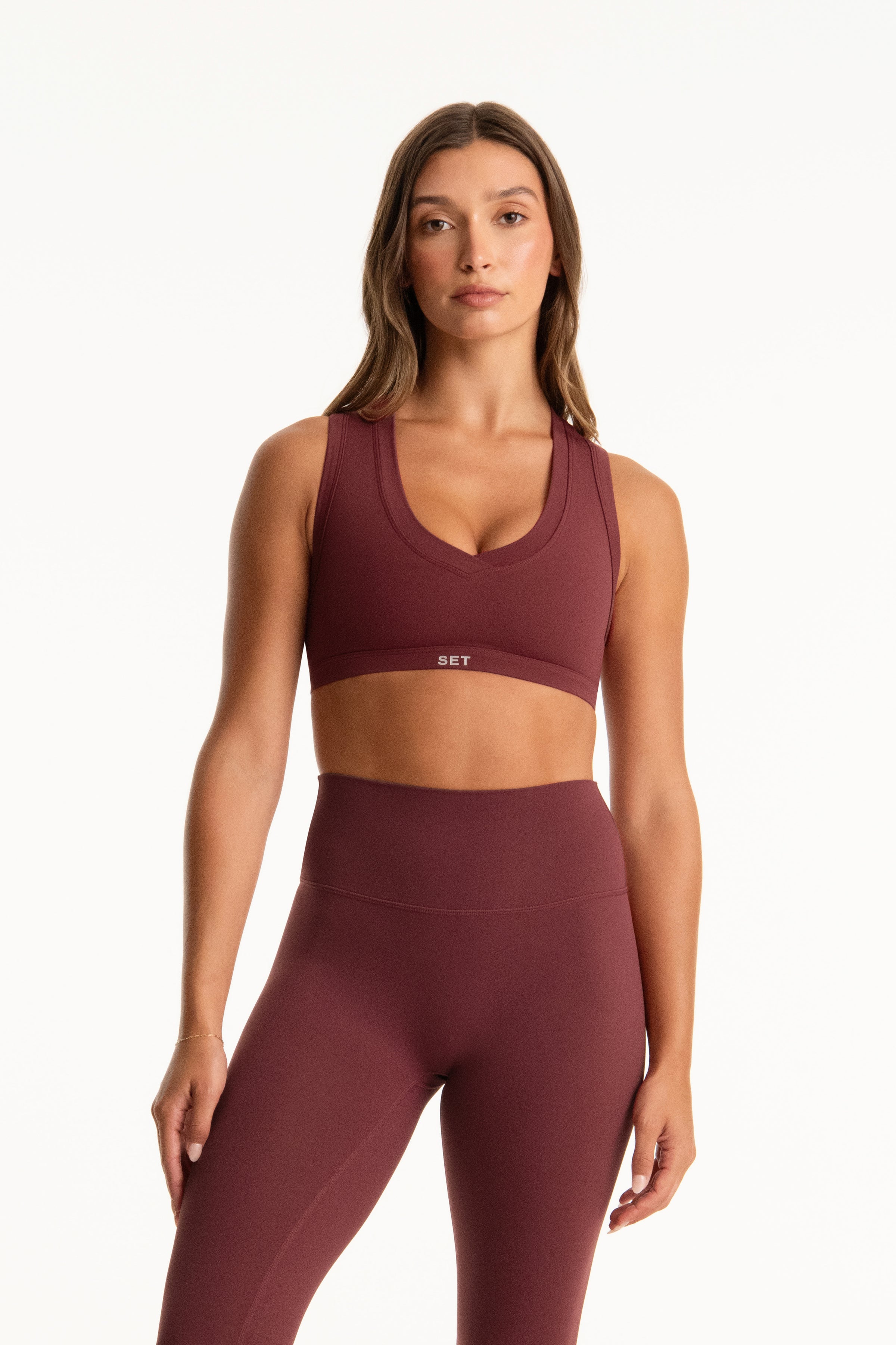 Woman wearing a maroon sports bra and leggings set on a white background 