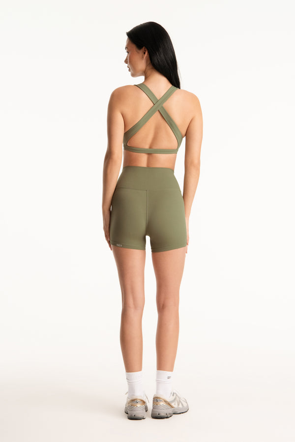 Woman wearing a green sports bra and shorts on a white background