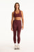 Woman wearing a maroon sports bra and leggings set on a white background