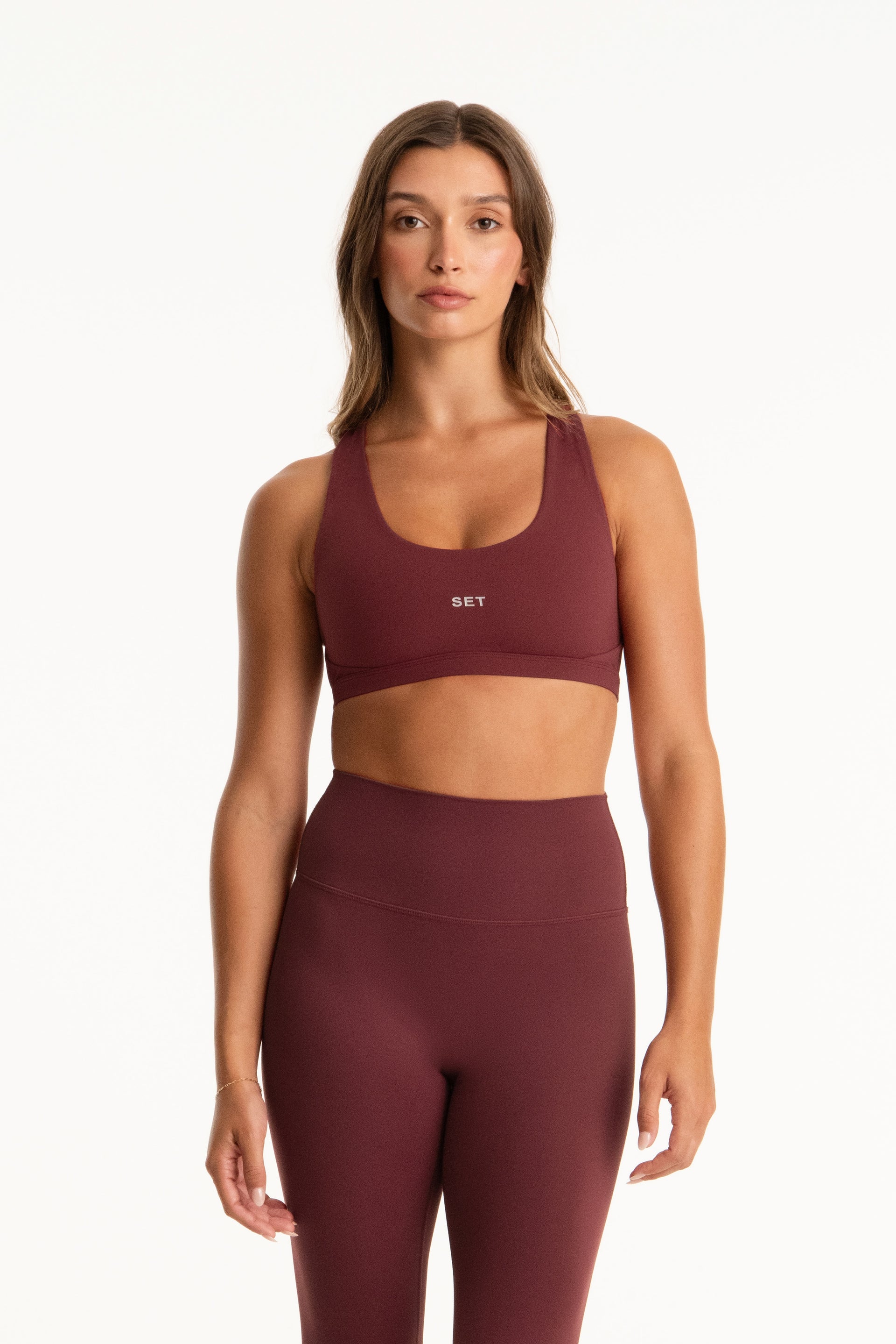 Woman wearing a maroon sports bra and leggings set on a white background <model-info>Presley wears a size S and is 5’6”, 26” waist, 33” bust.</model-info>