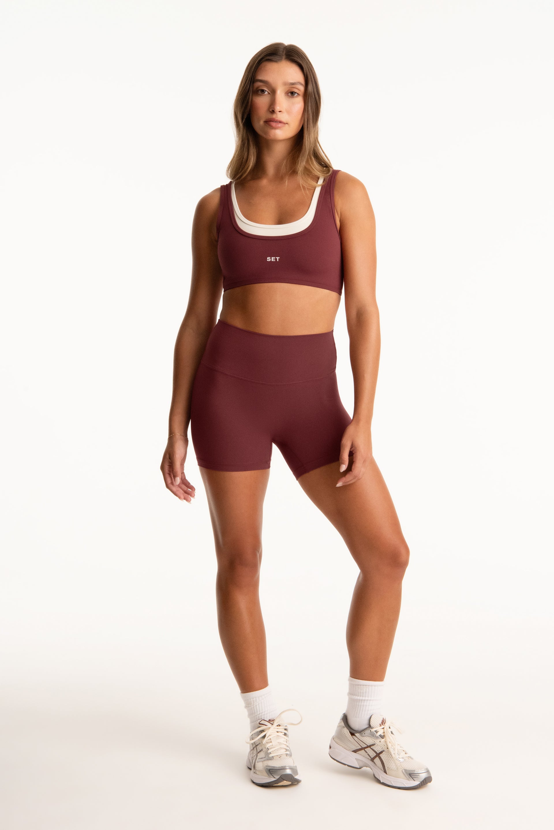 Woman wearing a maroon sports bra and shorts set on a white background