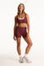 Woman wearing a maroon sports bra and shorts set on a white background
