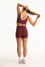 Woman wearing a maroon sports bra and shorts on a white background