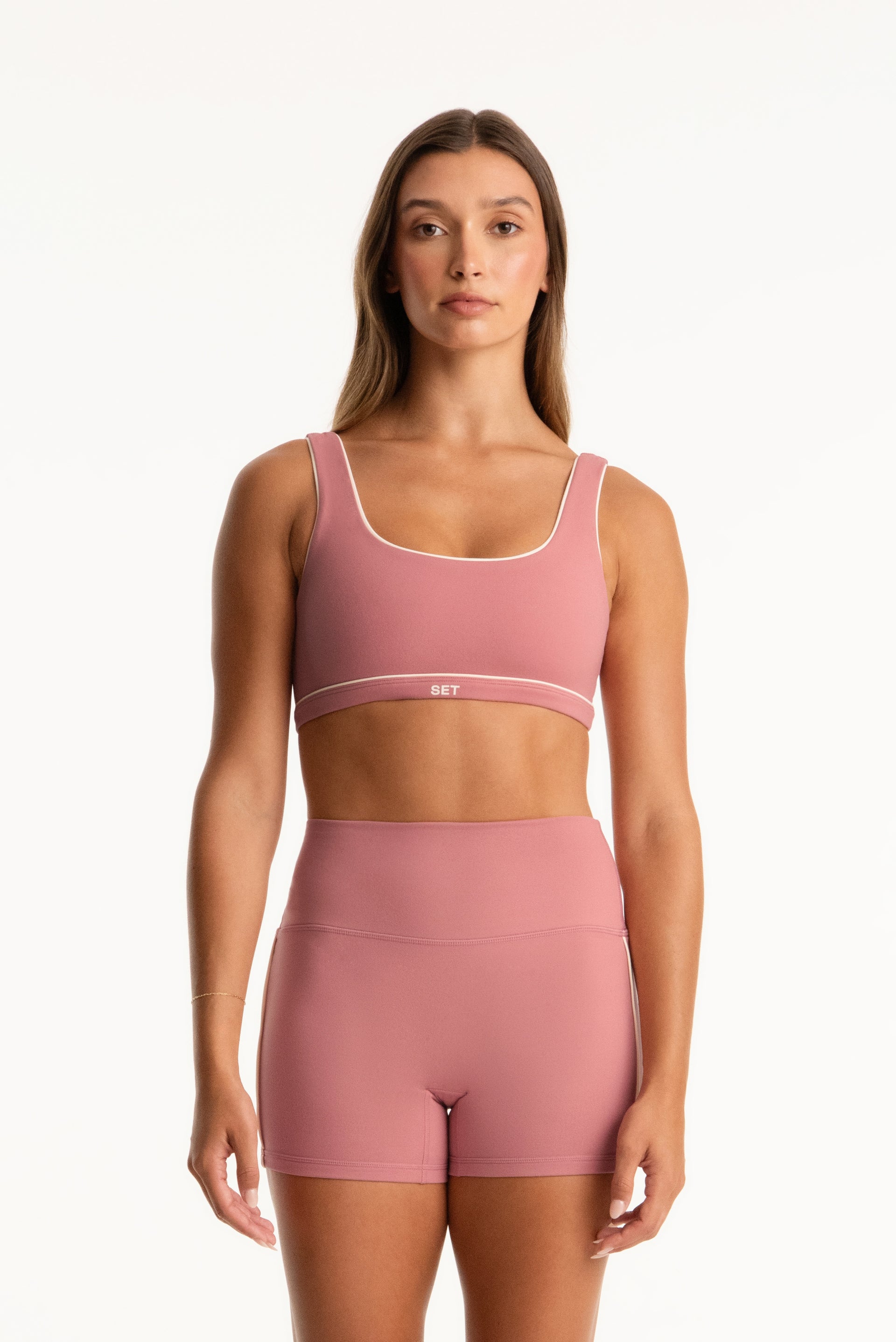 Woman wearing a pink sports bra and shorts set on a white background <model-info>Presley wears a size S and is 5’6”, 26” waist, 33” bust.</model-info>