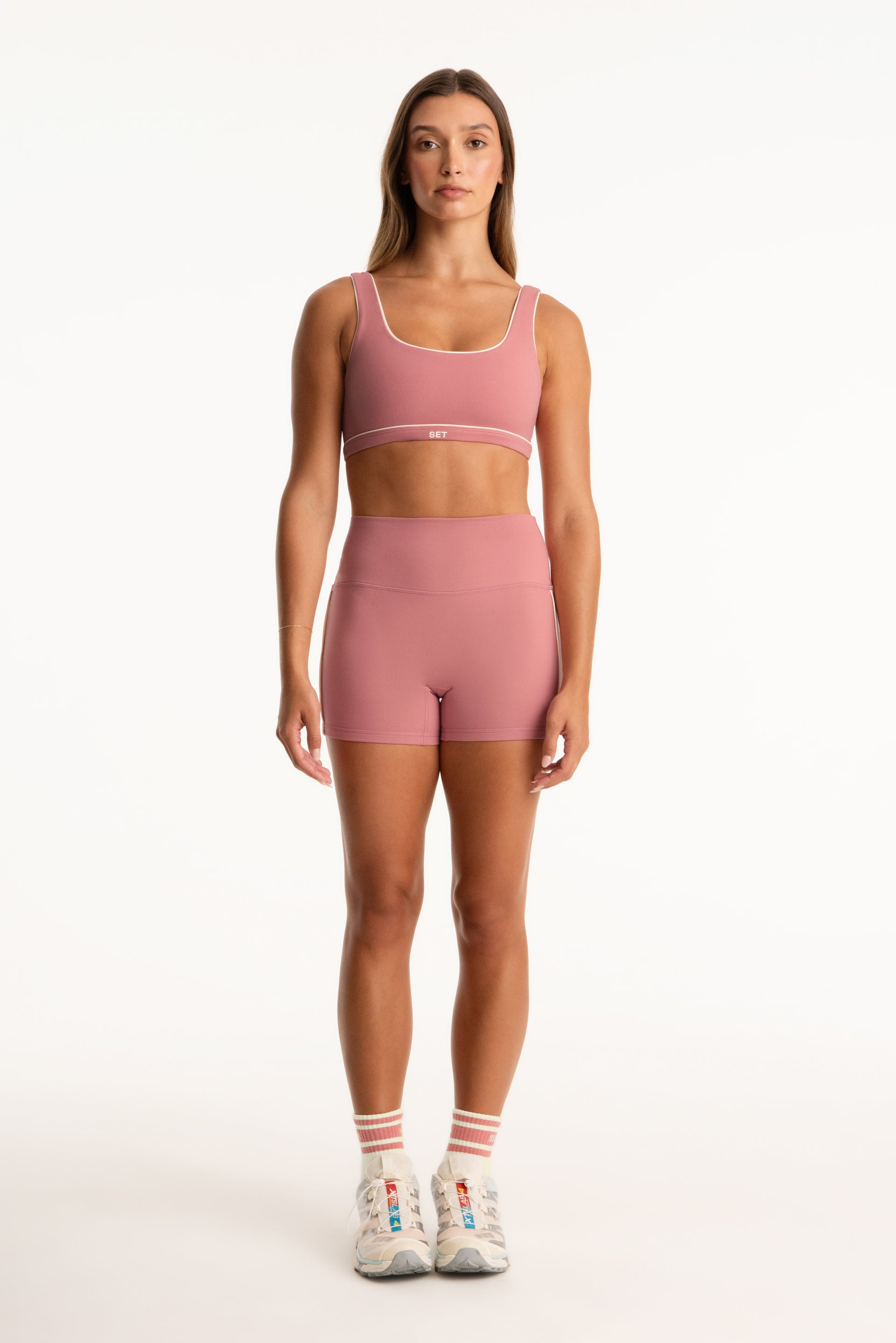 Woman wearing a pink sports bra and shorts set on a white background