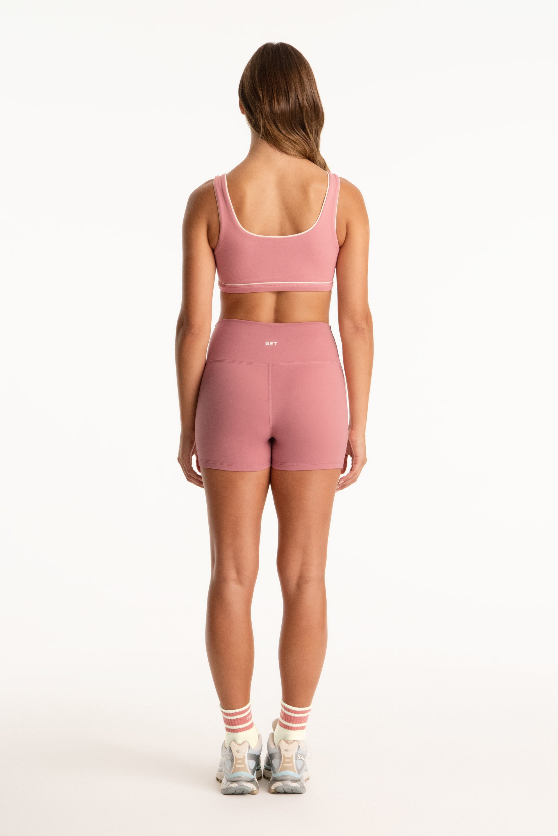 Person wearing a pink sports bra and shorts set on a white background