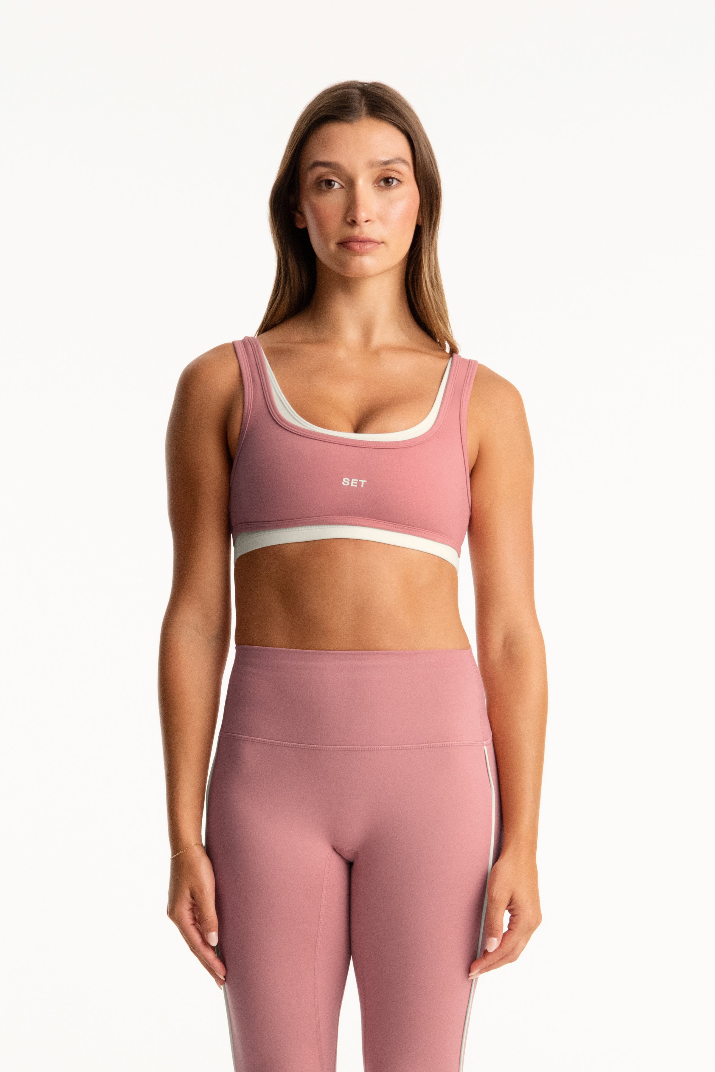 Woman wearing a pink sports bra and leggings set on a white background 