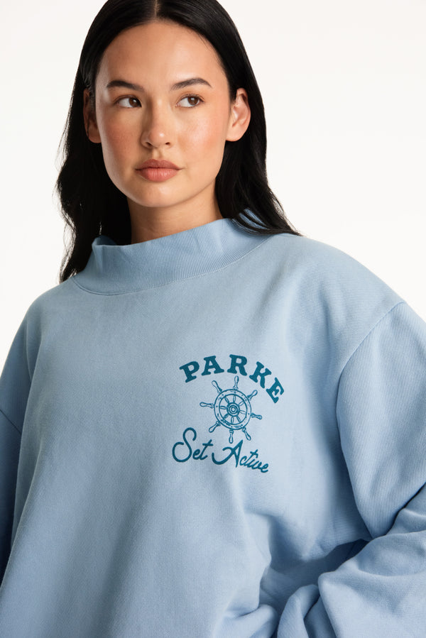 Person wearing a light blue sweatshirt with 'Parke Set Acre' branding on a white background