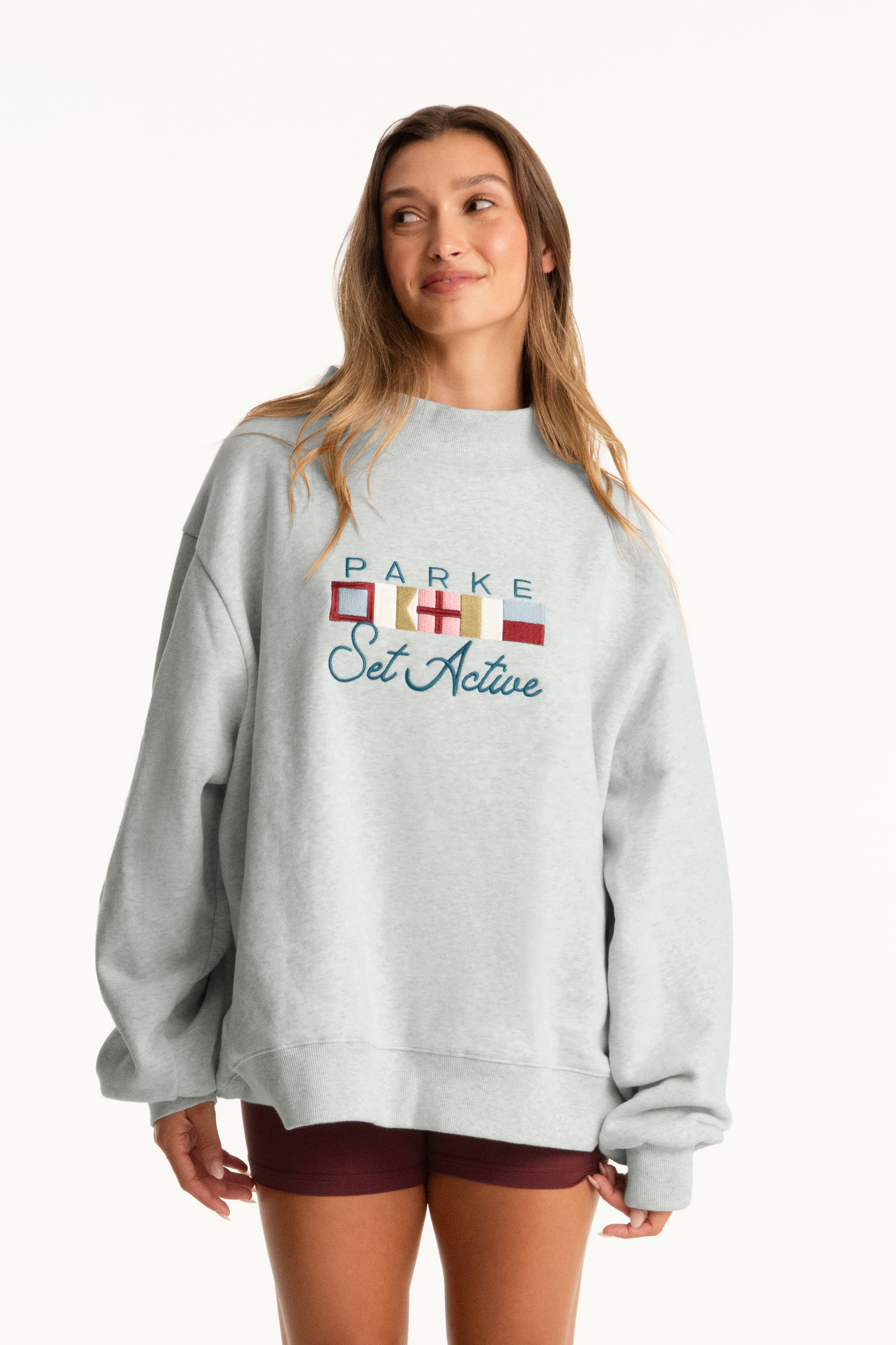 Woman wearing a gray sweatshirt with colorful text on a white background <model-info>Presley wears a size L/XL and is 5’6”, 26” waist, 33” bust.</model-info>
