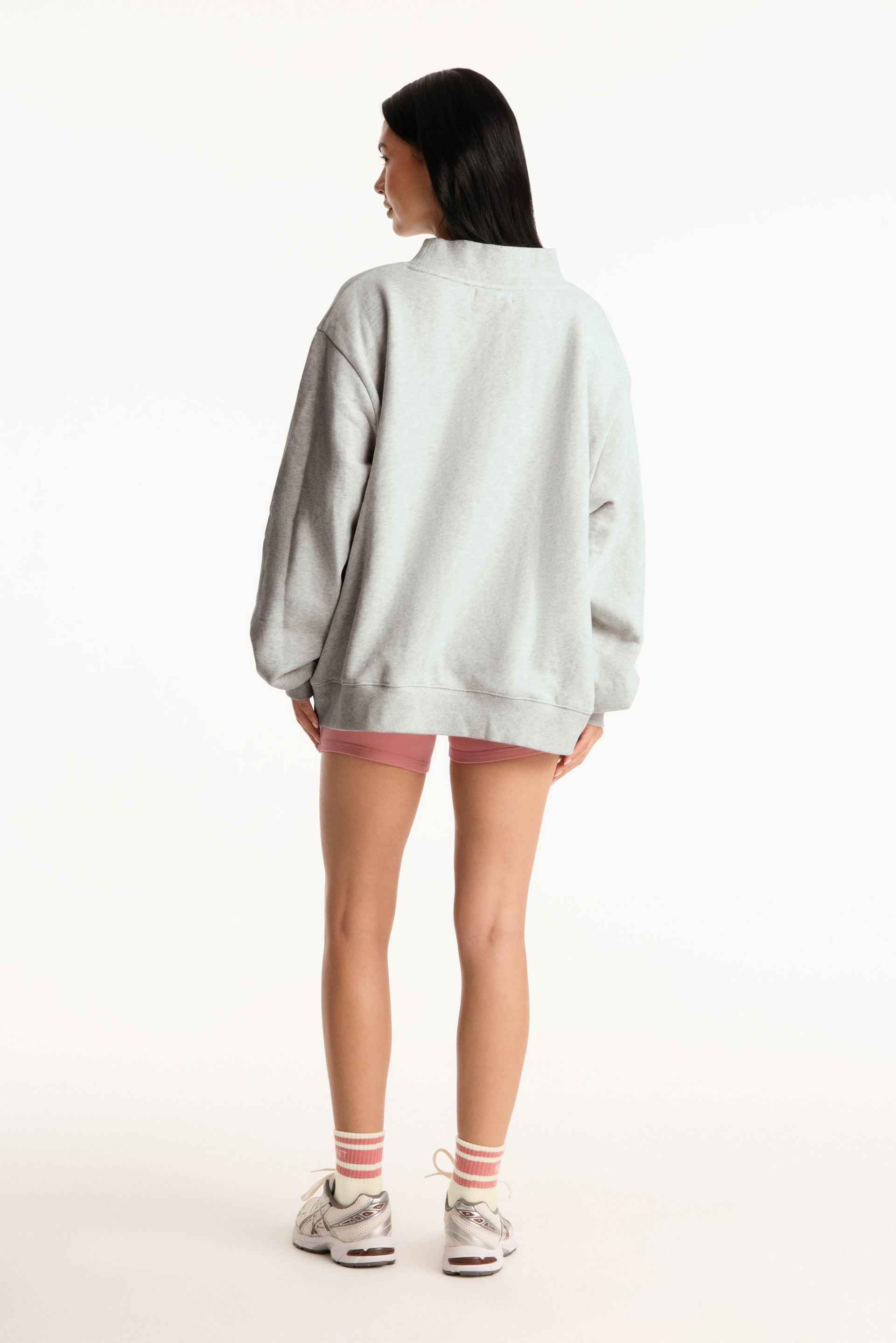Person wearing a light gray oversized sweatshirt and pink shorts on a white background