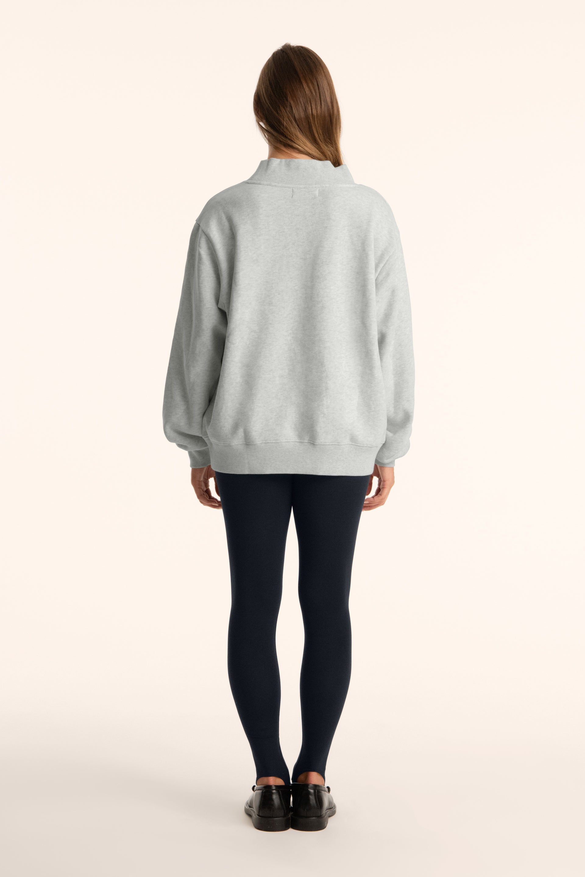 Person wearing a light gray sweatshirt and black leggings on a white background