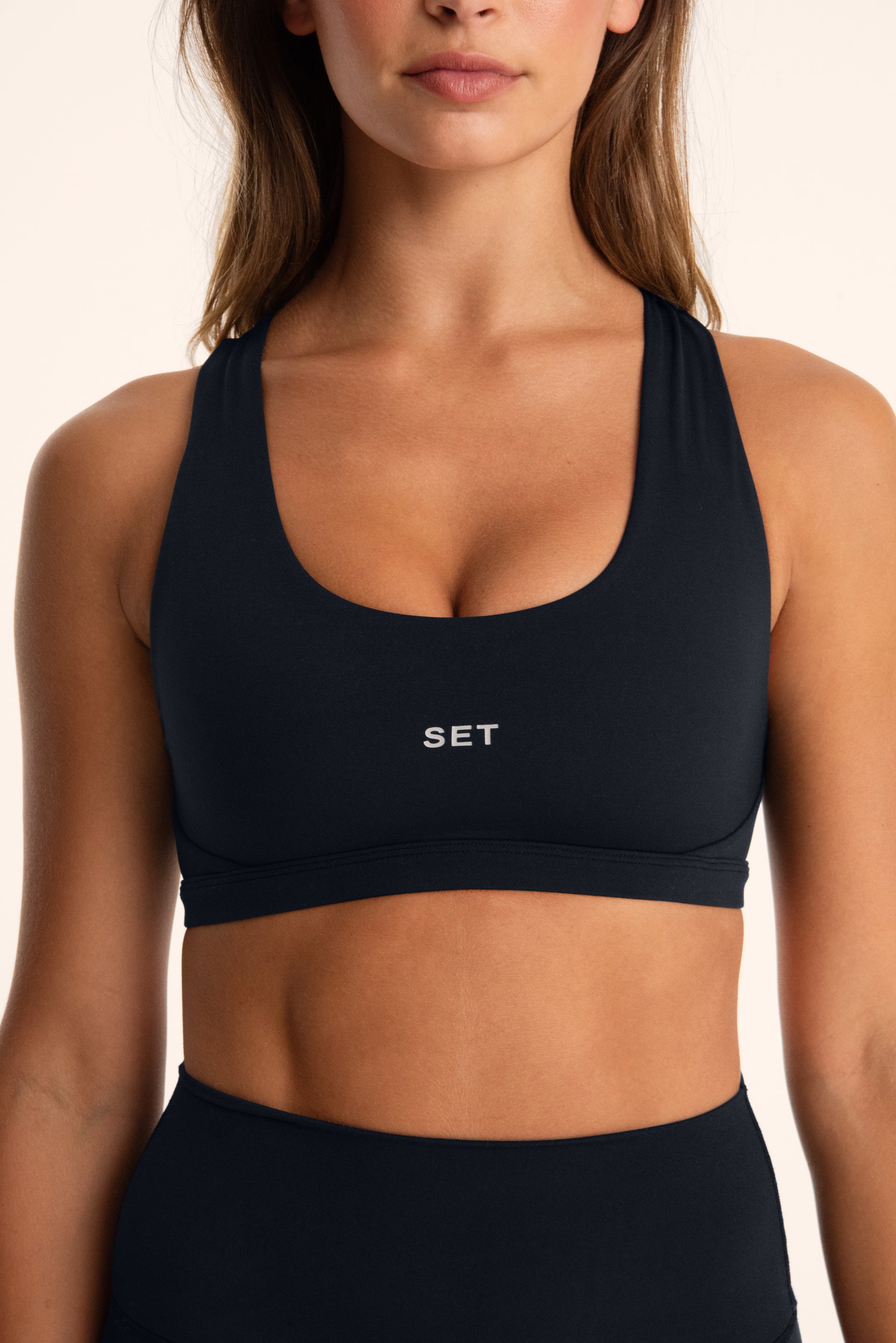 Black sports bra with 'SET' logo worn by a person on a beige background