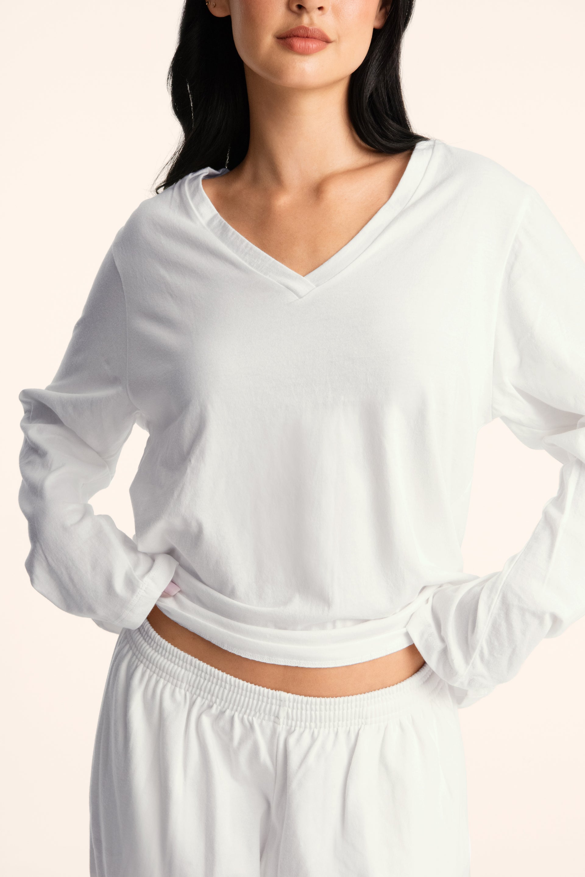 Woman wearing a white long-sleeve top and pants on a light background