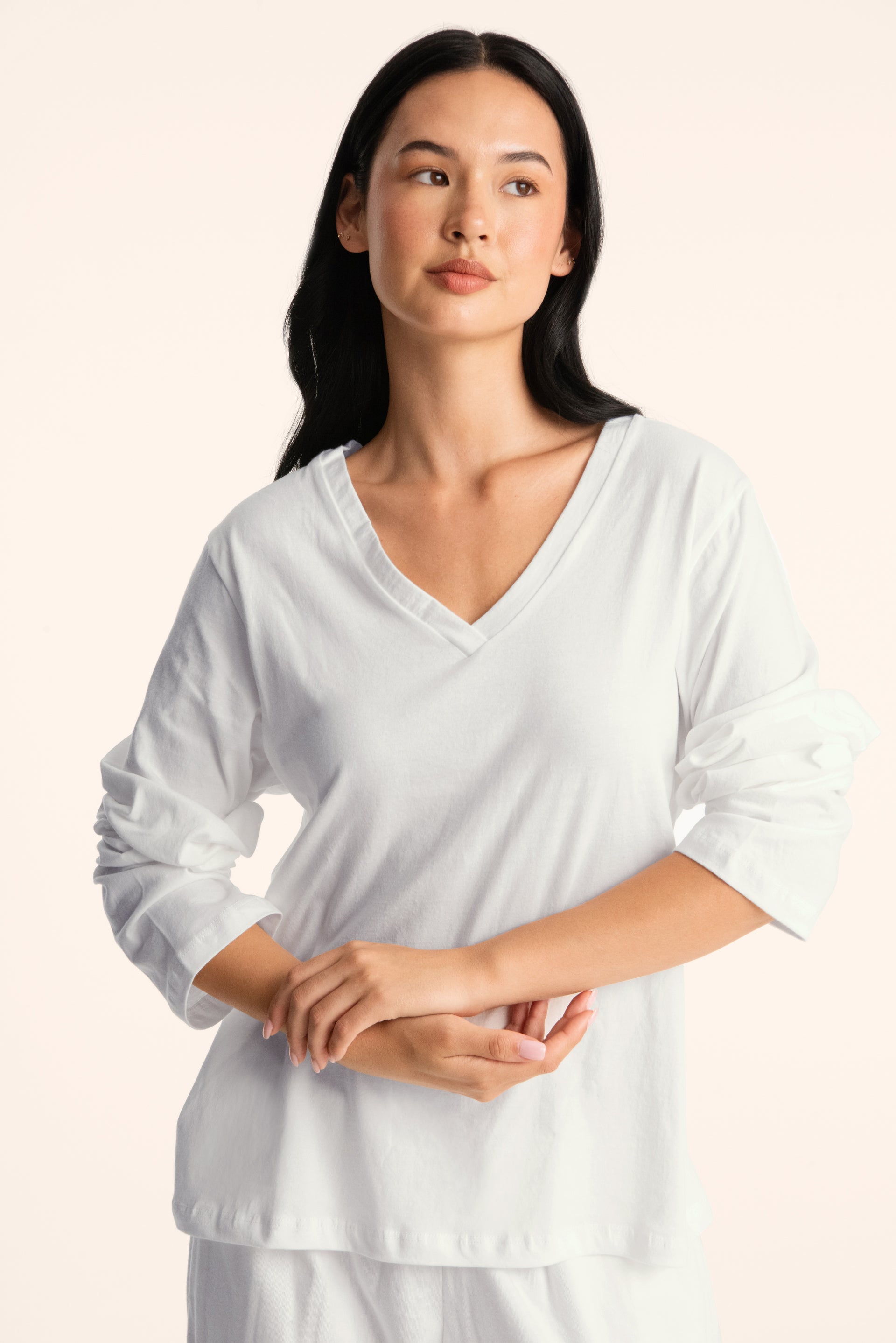 Woman wearing a white long-sleeve top with a V-neck on a light pink background <model-info>Jasmine wears a size S and is 5’8”, 25" waist, 36” bust.</model-info>