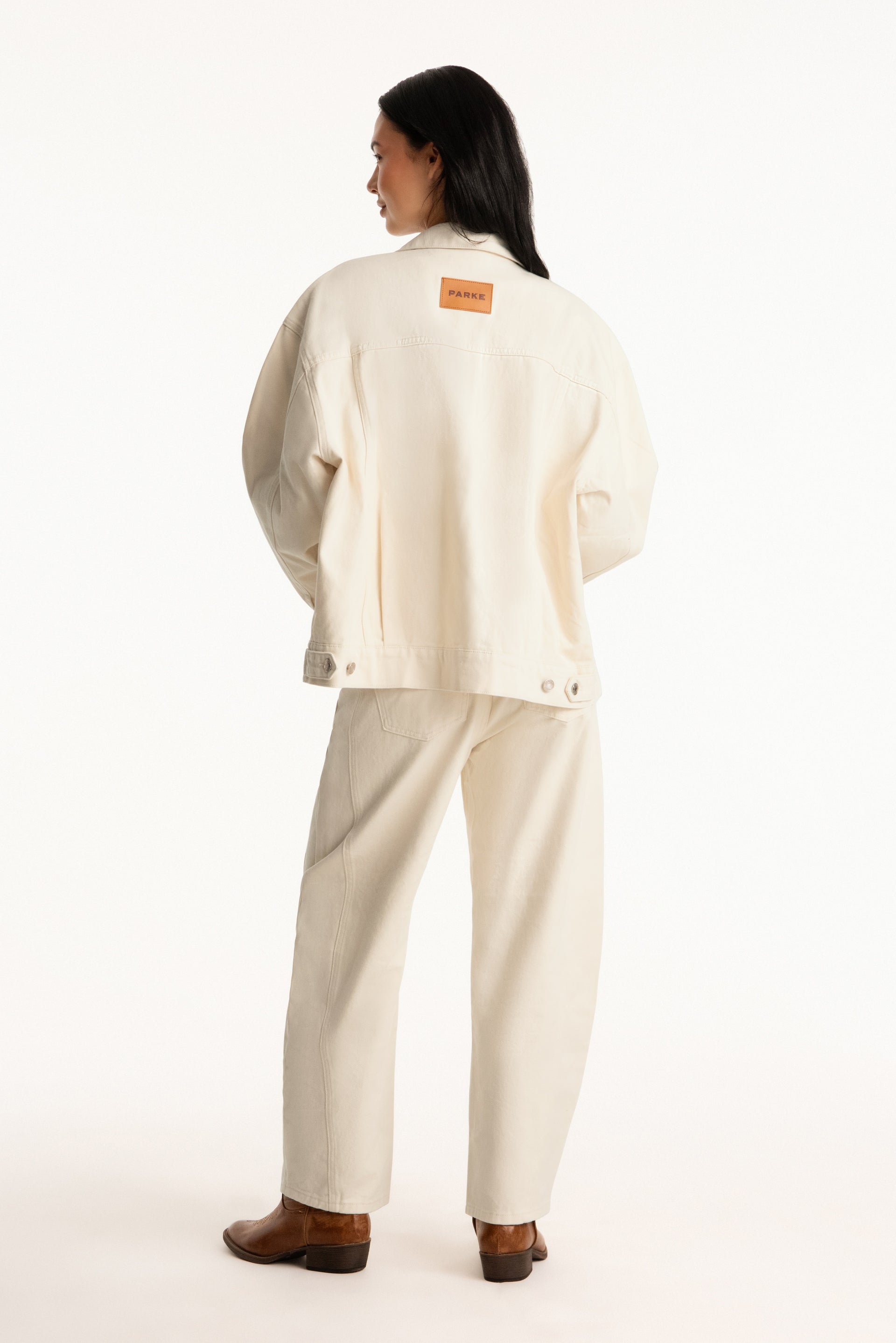 Person wearing a beige outfit with a logo on the back against a white background