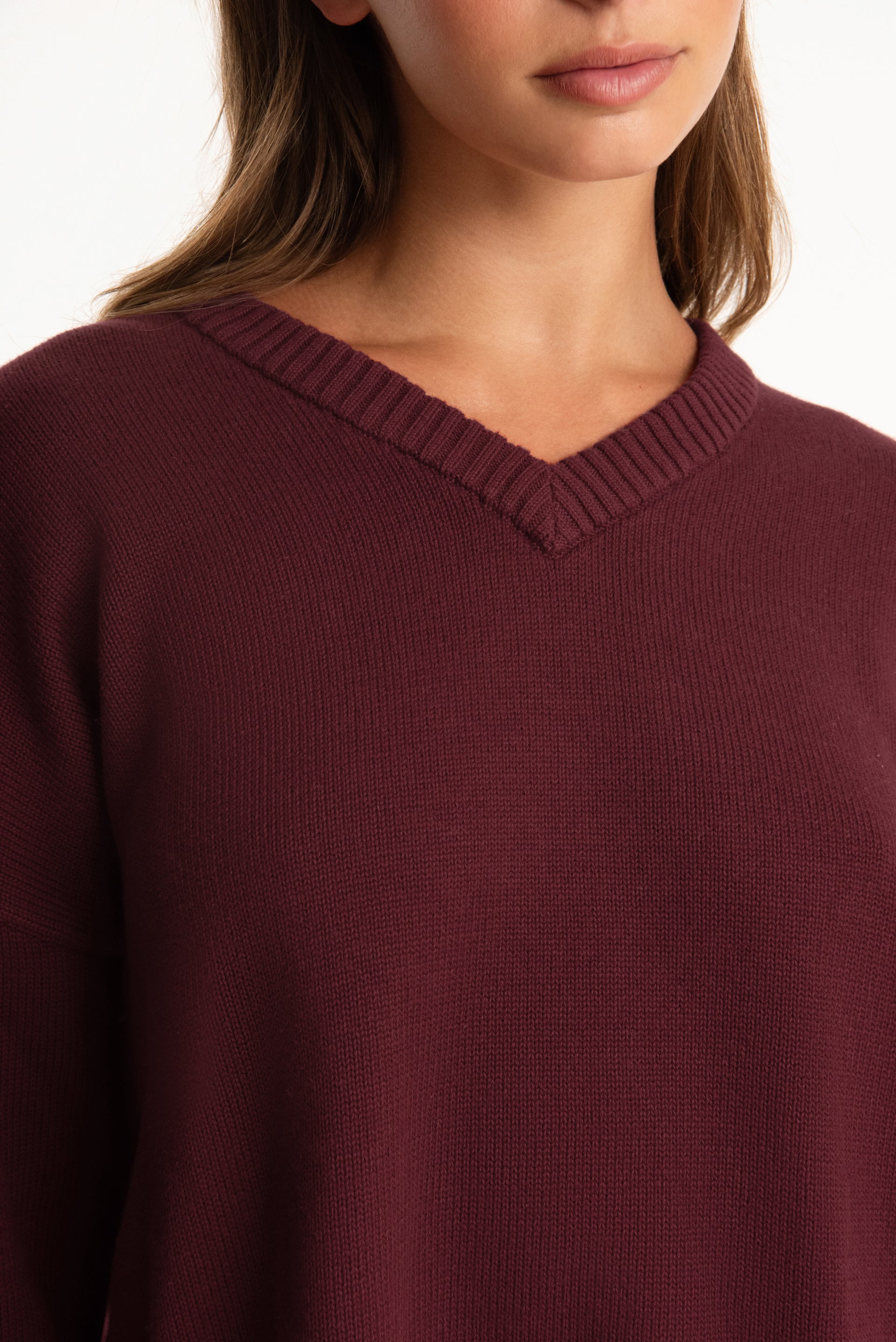 Close-up of a person wearing a burgundy sweater with a neutral background
