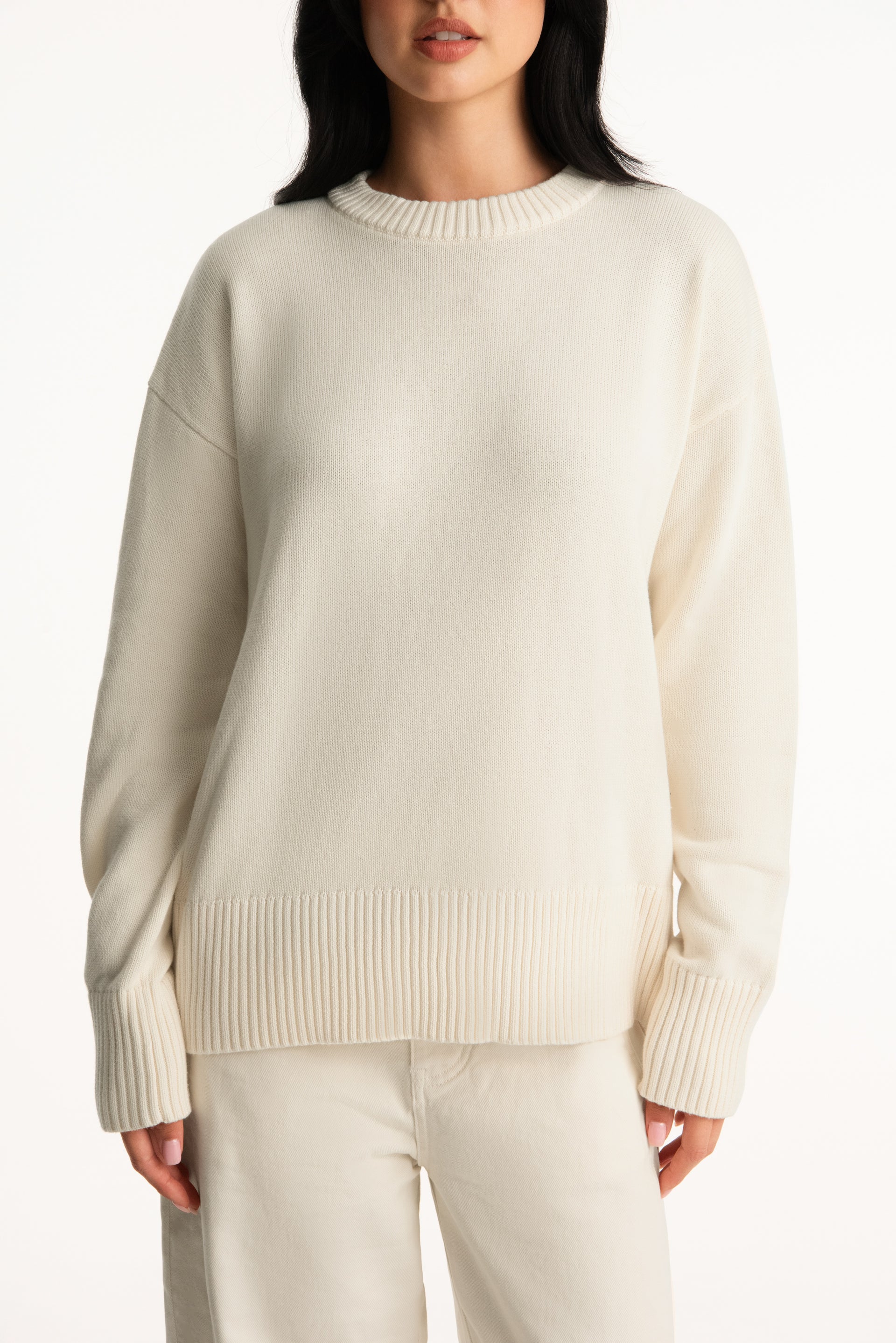 Person wearing a beige sweater and pants on a white background