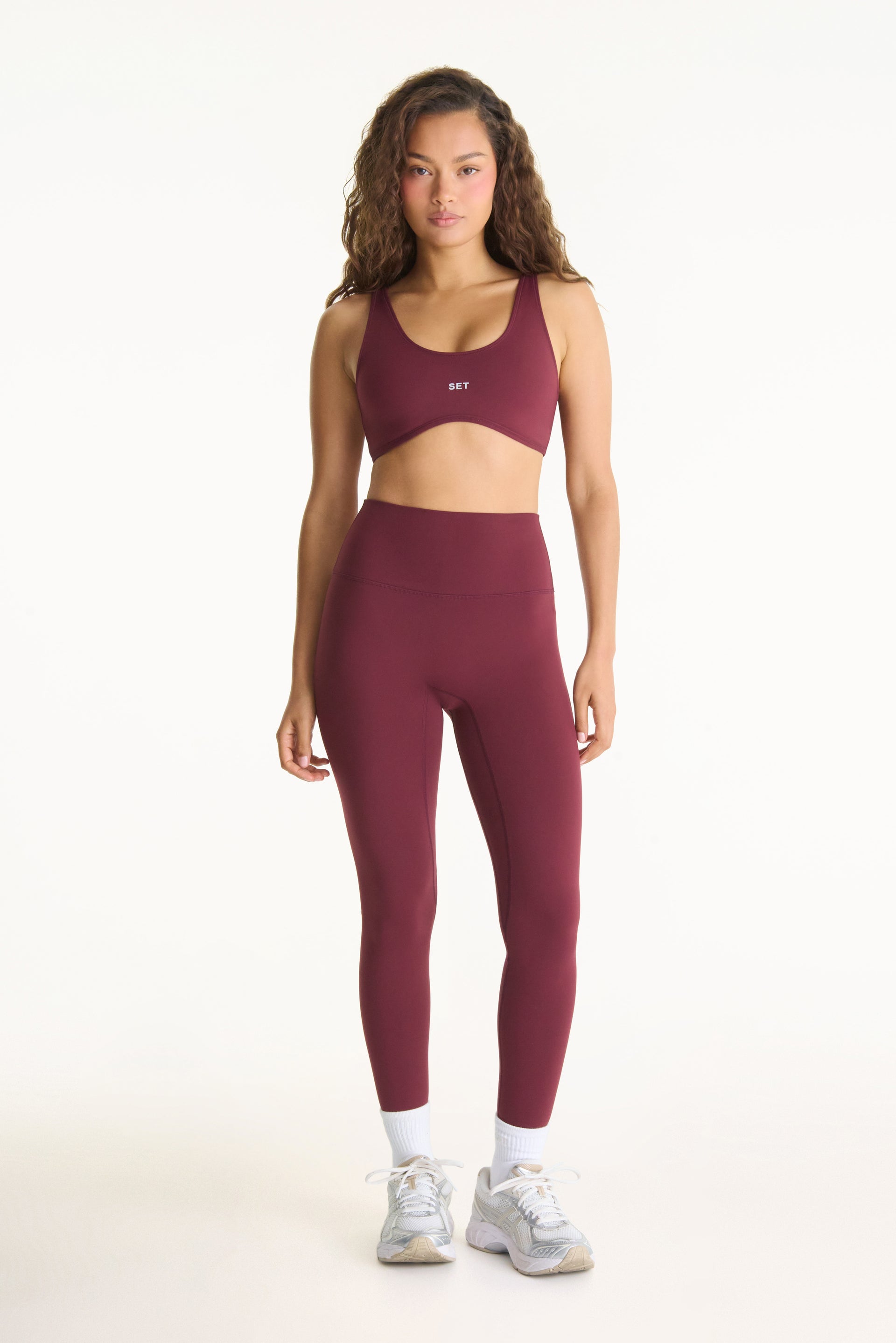 Woman wearing a maroon sports bra and leggings set on a white background
