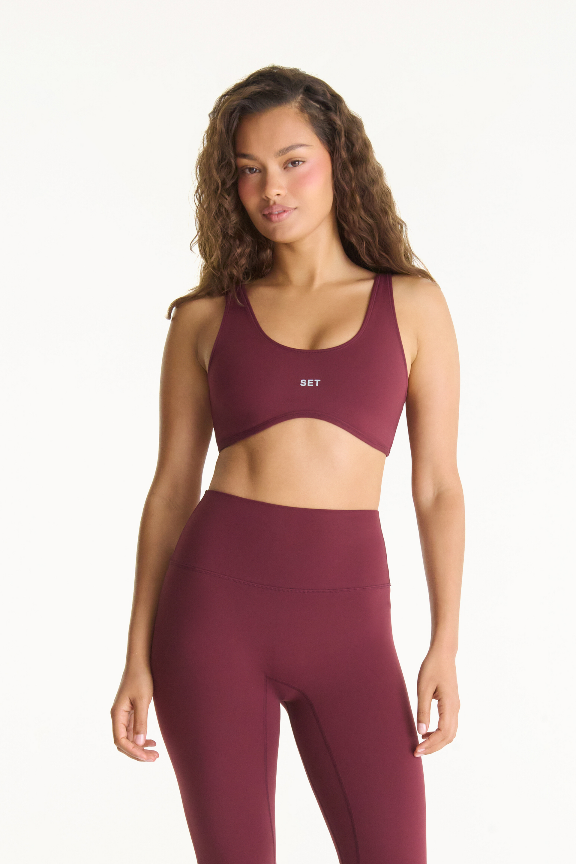 Woman wearing a maroon sports bra and leggings set on a white background <model-info>Jana wears a size S and is 5’4½”, 24” waist, 33½” bust.</model-info>