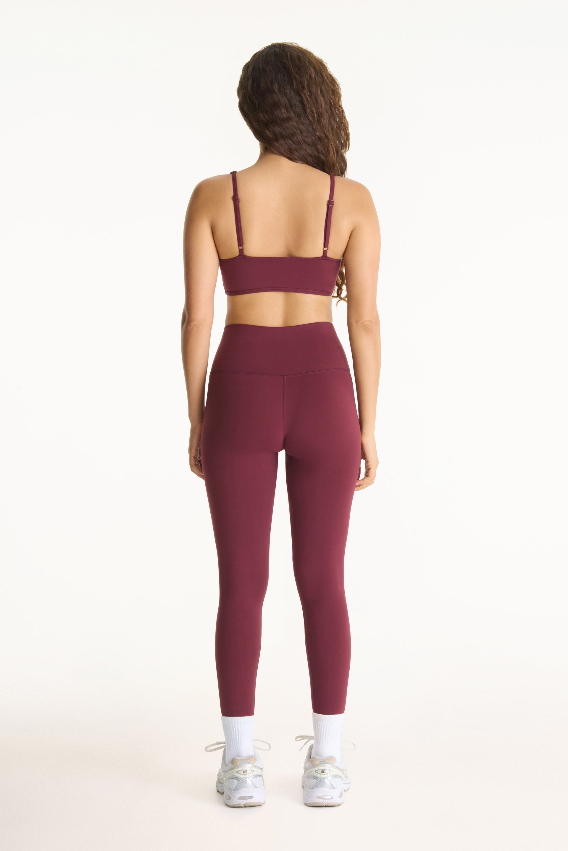 Person wearing a burgundy sports bra and leggings set on a white background