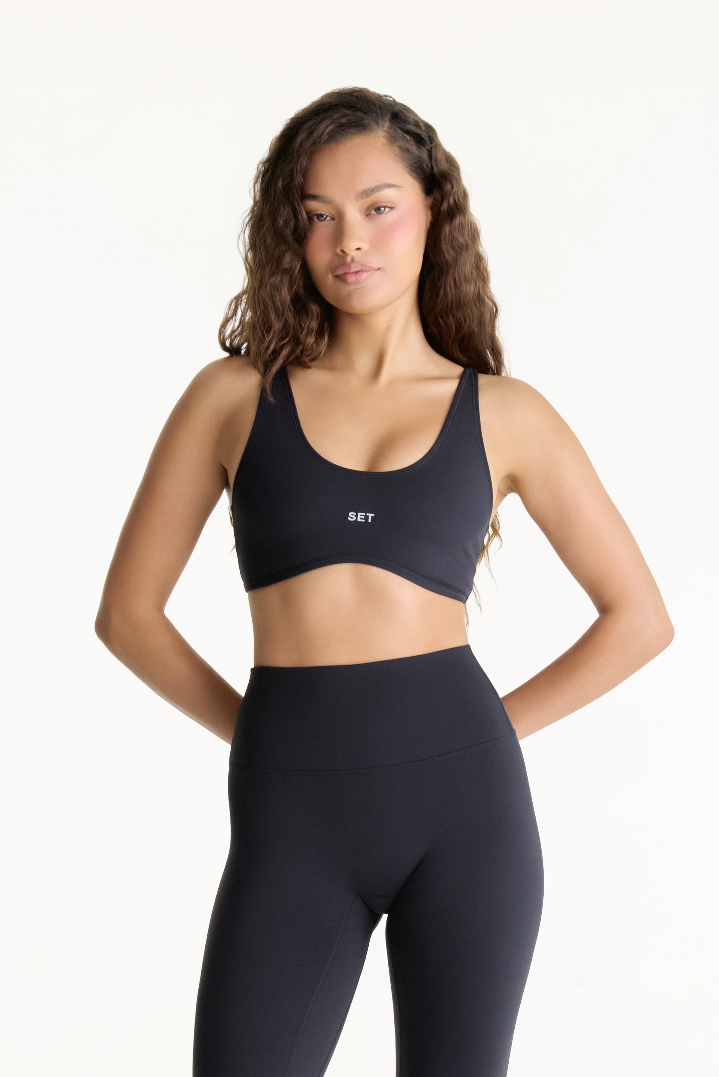 Woman wearing a black sports bra and leggings with 'SET' branding on a white background 