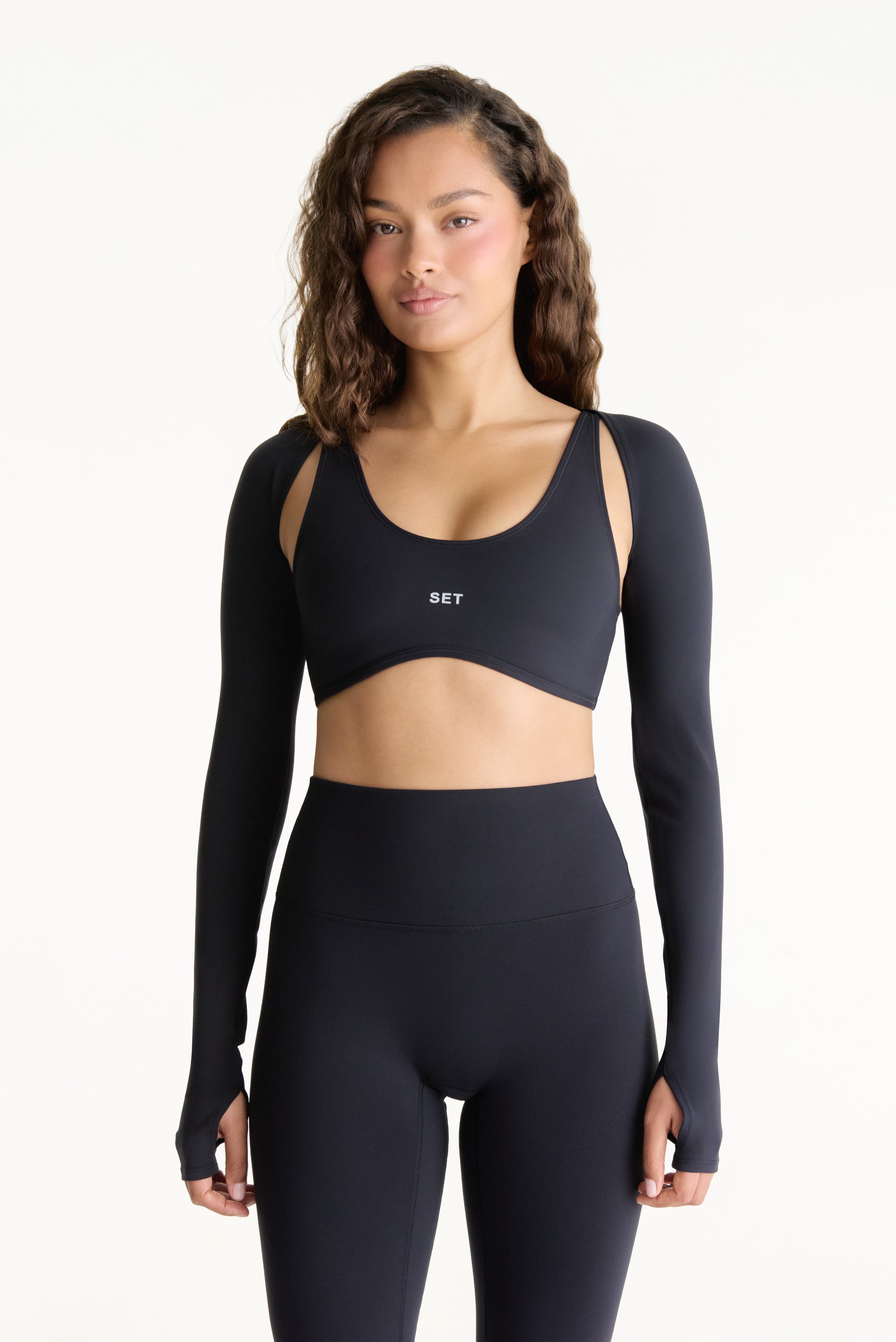 Woman wearing a black long-sleeve sports bra and leggings on a white background <model-info>Jana wears a size S and is 5’4½”, 24” waist, 33½” bust.</model-info>