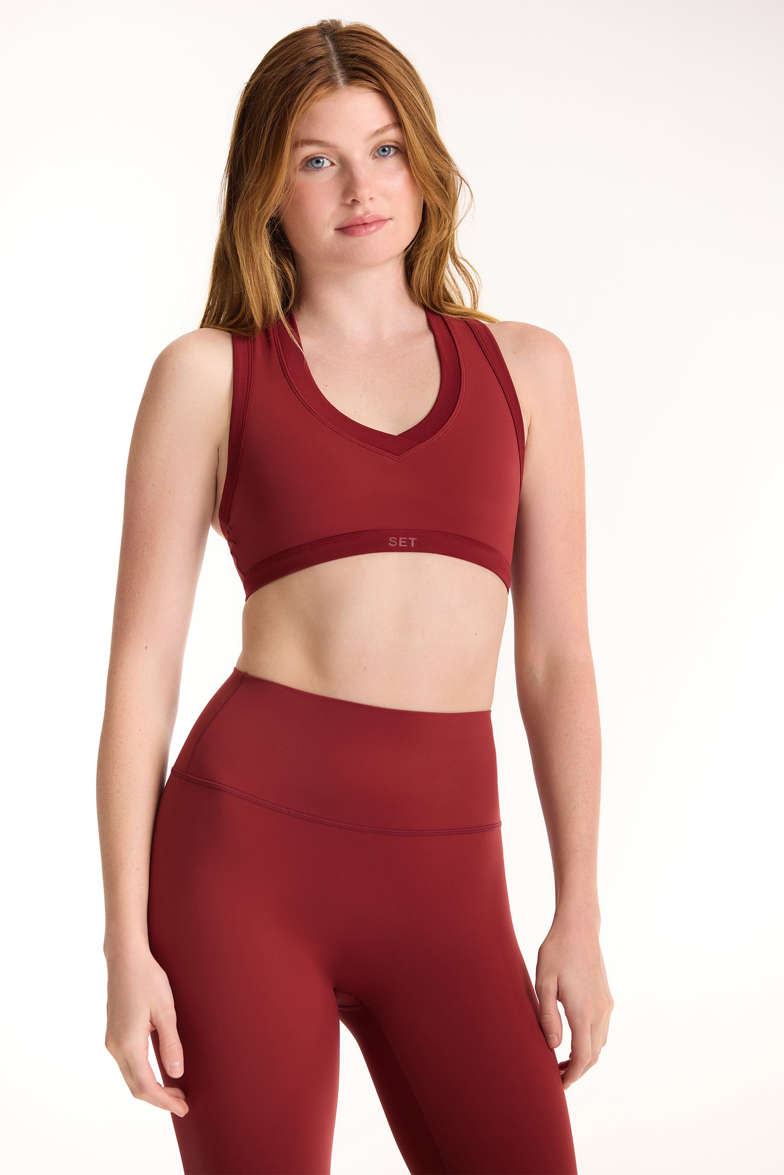 Woman wearing a red sports bra and leggings on a white background <model-info>Dickey wears a size S and is 5’9”, 24” waist, 32” bust.</model-info>