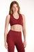 Woman wearing a red sports bra and leggings on a white background <model-info>Dickey wears a size S and is 5’9”, 24” waist, 32” bust.</model-info>