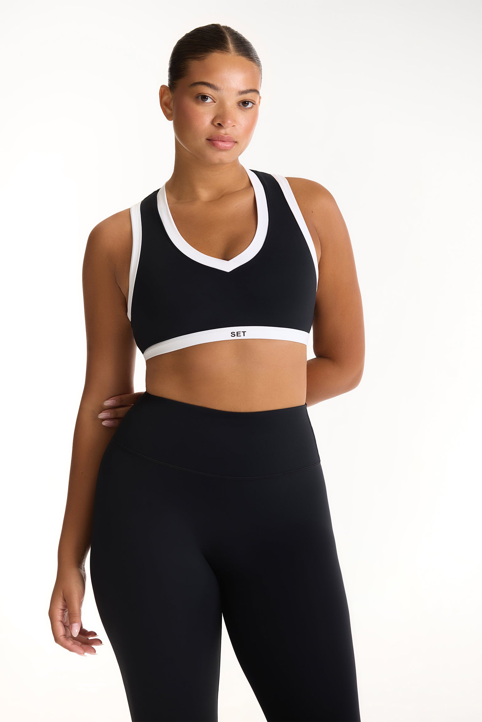 Woman wearing a black sports bra and leggings with a white brand logo on a white background 