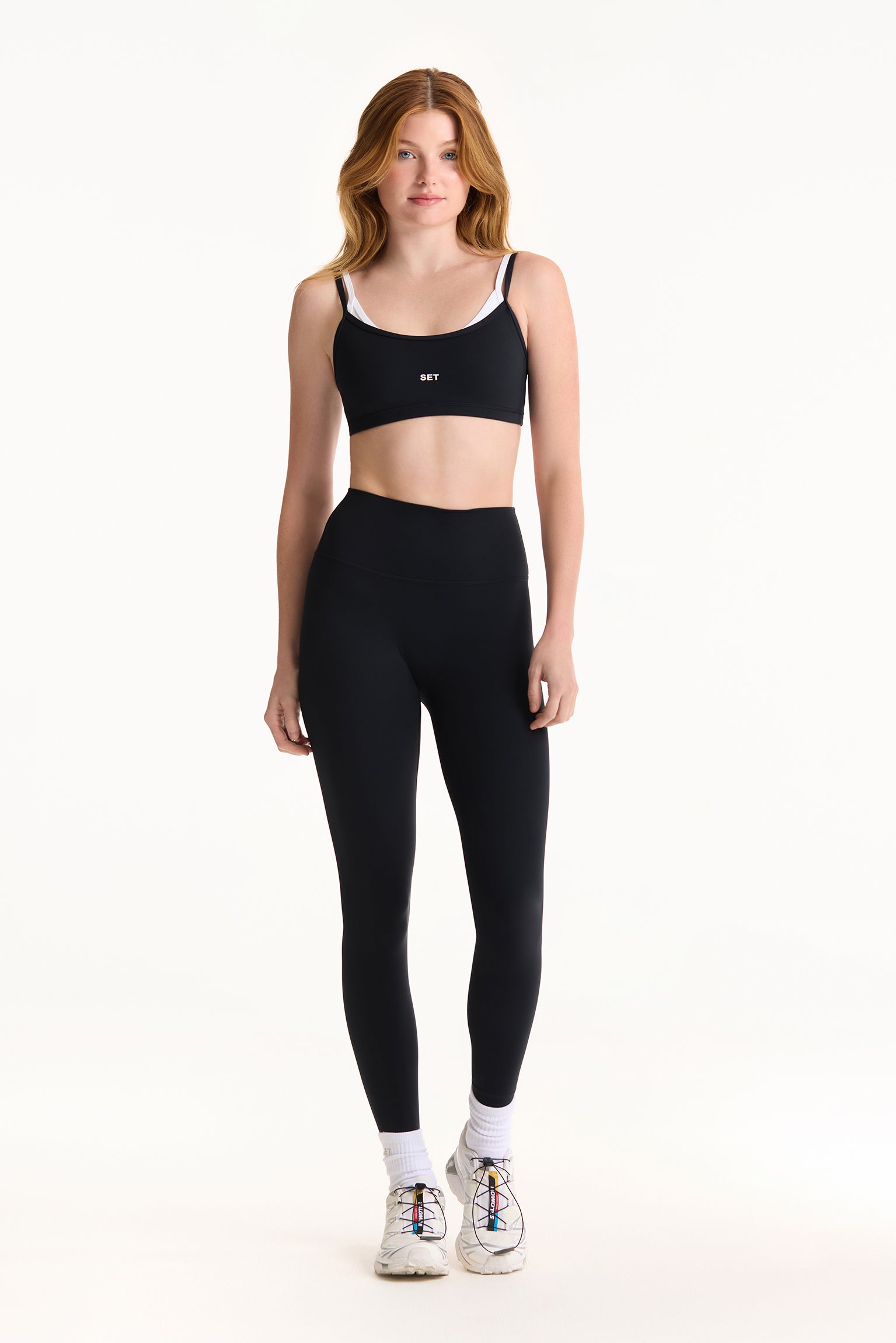 Woman wearing a black sports bra and leggings on a white background