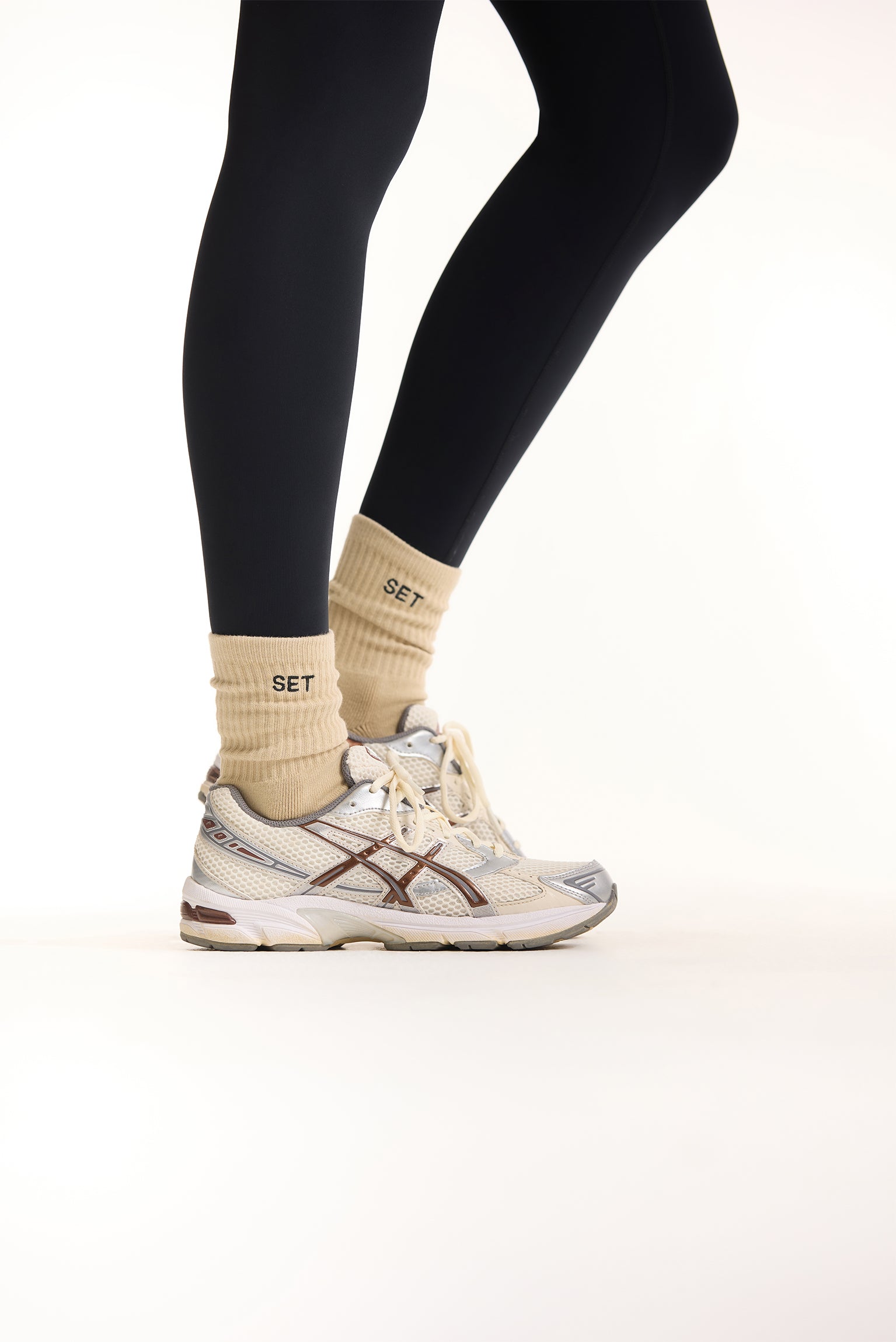 Person wearing black leggings, beige socks, and white sneakers on a light background