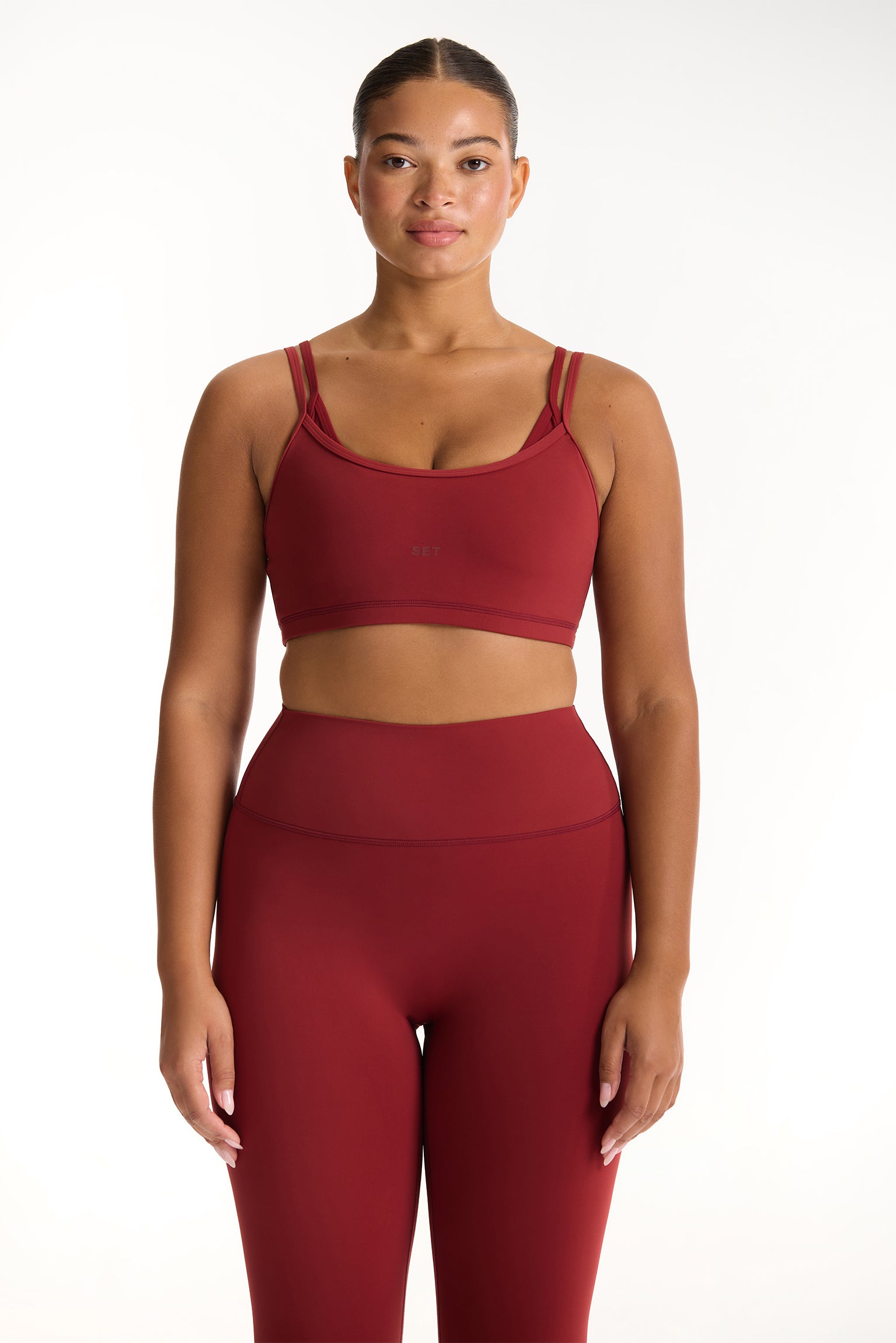 Woman wearing a red sports bra and leggings set on a white background <model-info>Jade wears a size L and is 5’9”, 30” waist, 38” bust.</model-info>