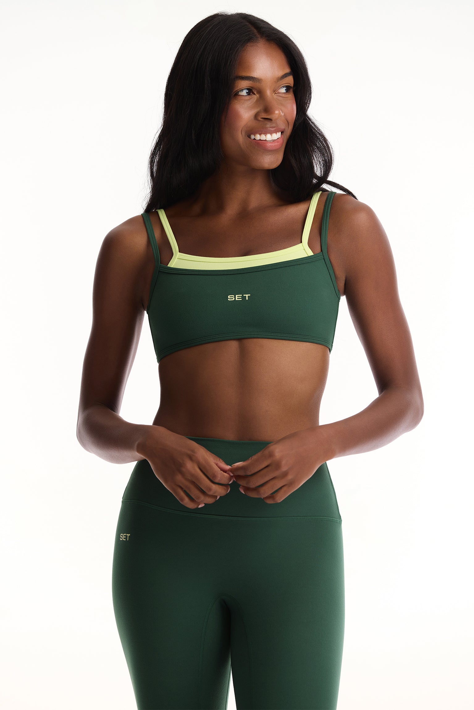 Woman wearing a green sports bra and leggings with a white background <model-info>Autumn wears a size S and is 5’7½“, 25" waist, 32" bust.</model-info>