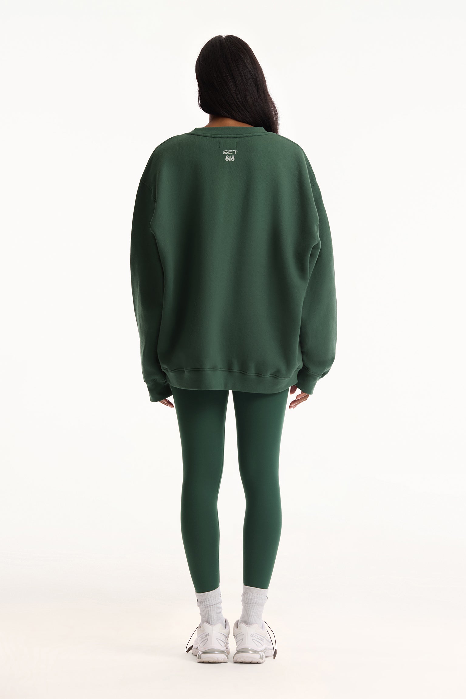 Person wearing a green sweatshirt and leggings on a white background