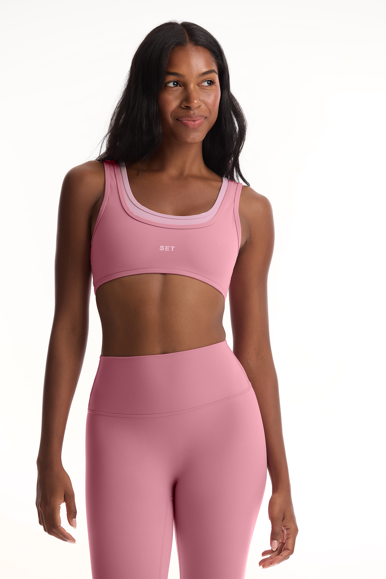 Woman wearing a pink sports bra and leggings set on a white background