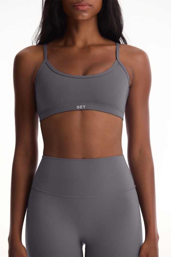 Woman wearing a gray sports bra and leggings set on a white background