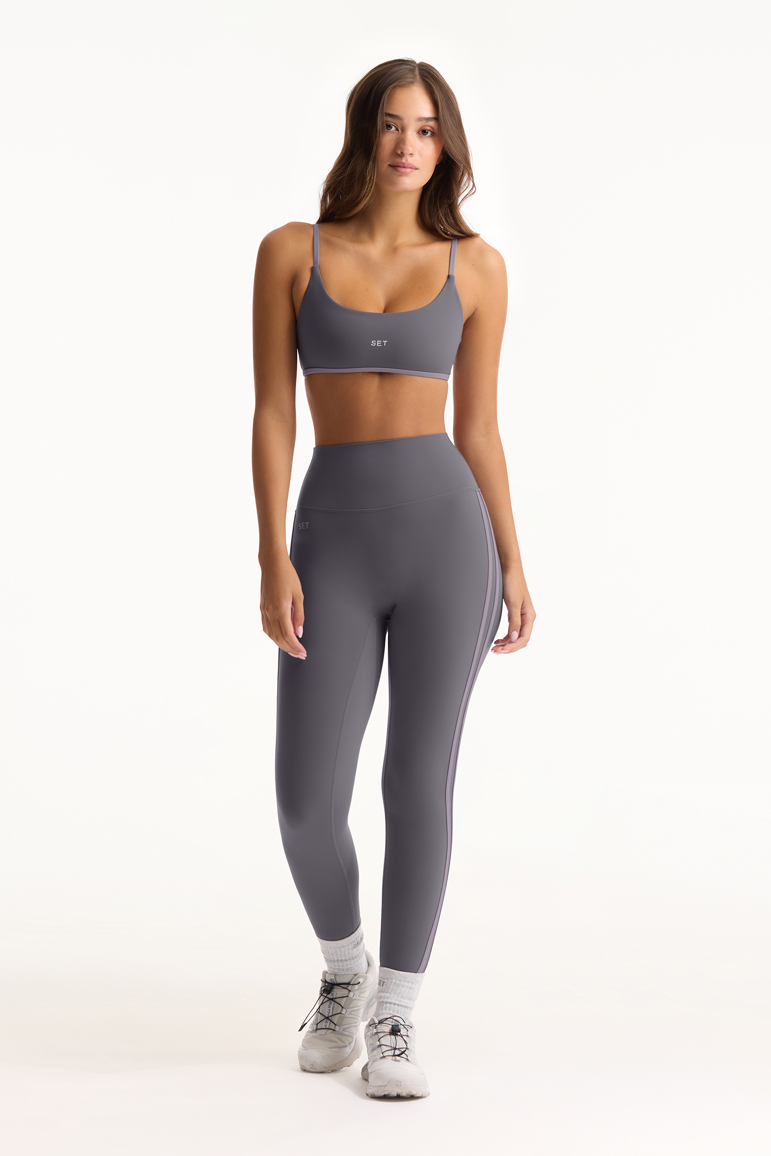 Woman wearing a gray sports bra and leggings set on a white background