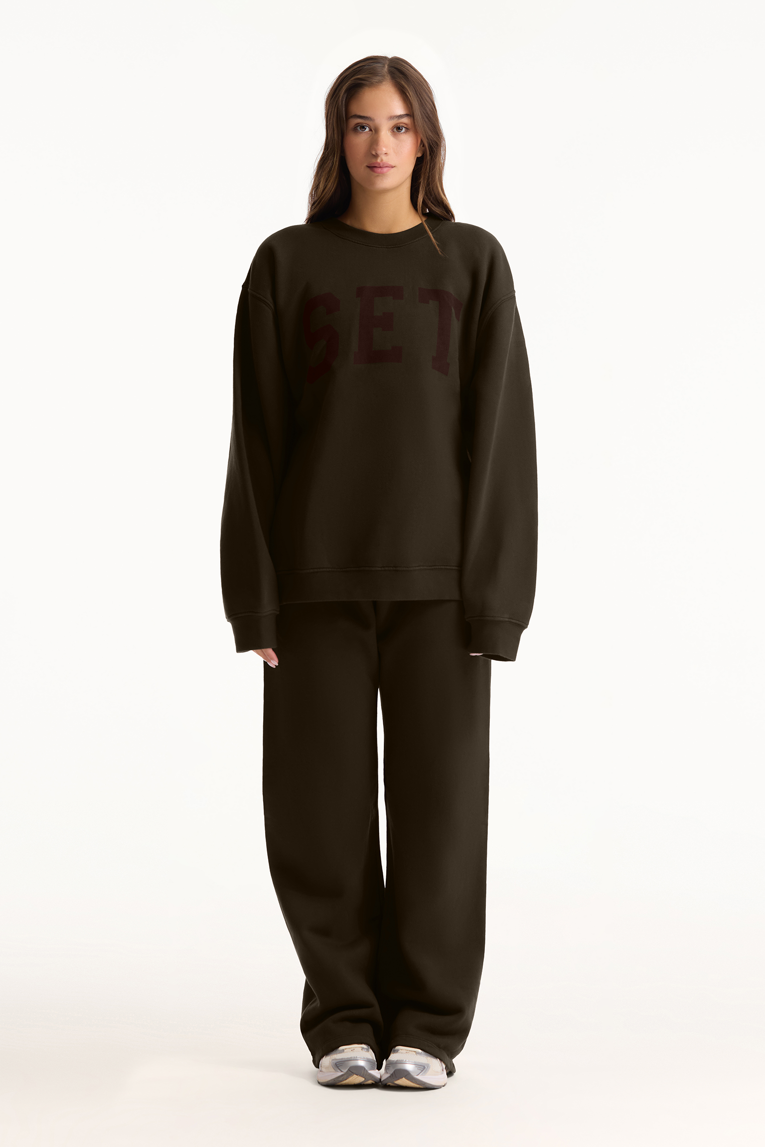 Person wearing a dark brown sweatshirt and pants on a white background