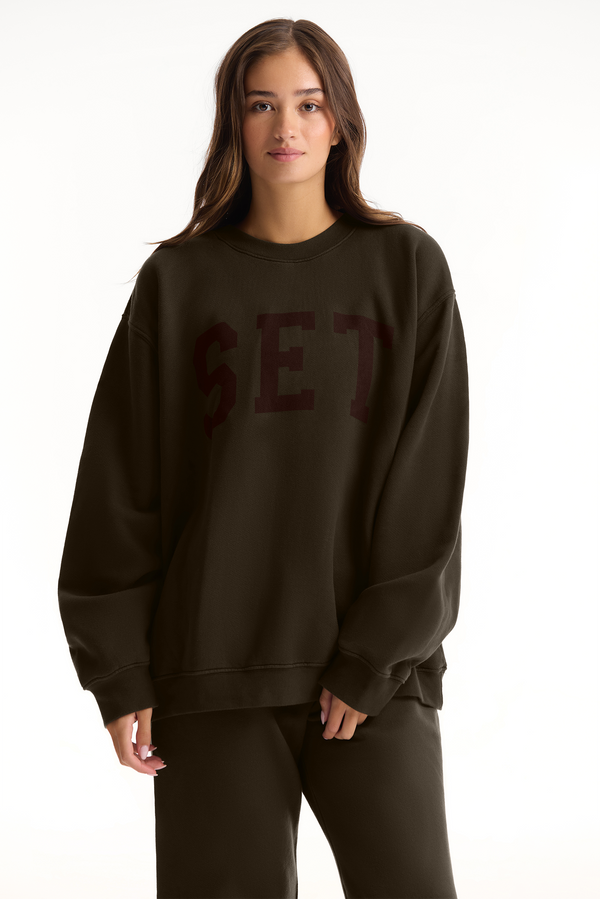 Person wearing a dark brown sweatshirt with 'SET' text on a white background 
