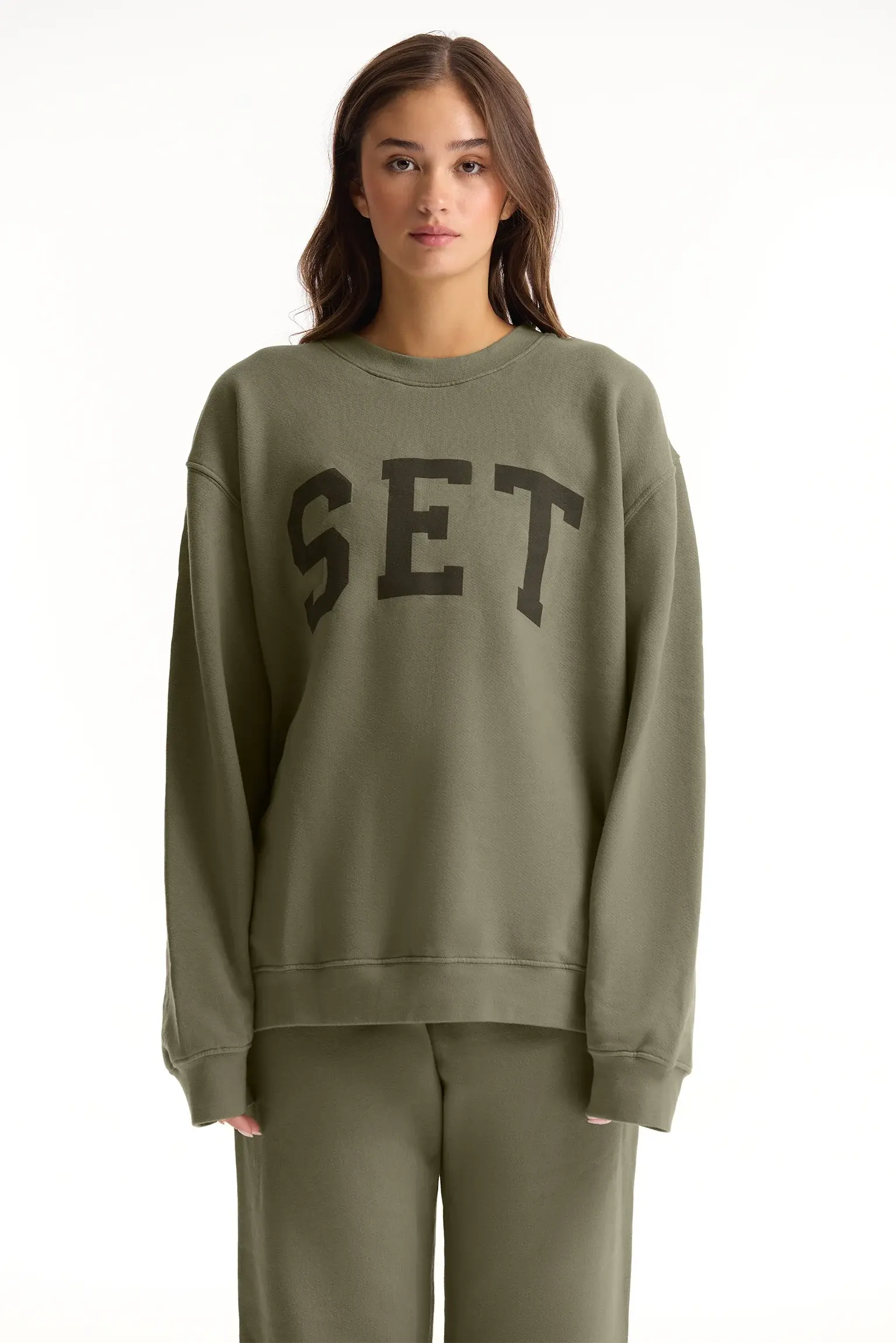 Person wearing a green sweatshirt with 'SET' text on a white background <model-info>Sophie wears a size L and is 5’9½”, 23” waist, 34CD bust.</model-info>
