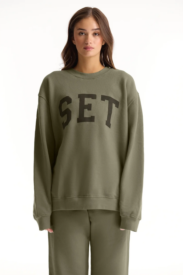 Person wearing a green sweatshirt with 'SET' text on a white background 