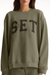 Person wearing a green sweatshirt with 'SET' printed on it against a white background