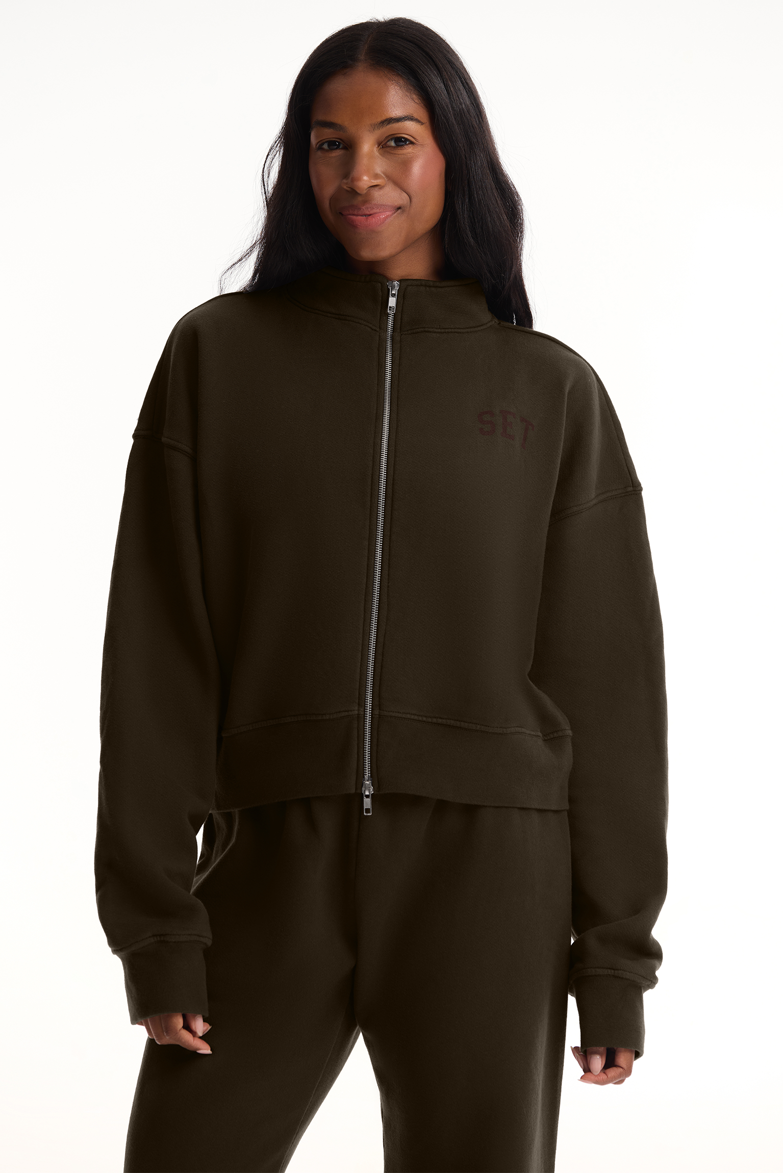Person wearing a dark brown tracksuit with a brand logo on a white background <model-info>Autumn wears a size M and is 5’7½”, 25” waist, 32” bust.</model-info>